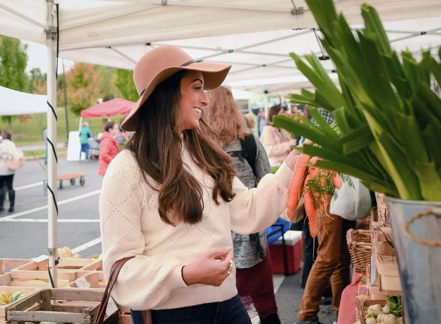 Woman shopping for vegetables at an outdoor market, holding carrots.
