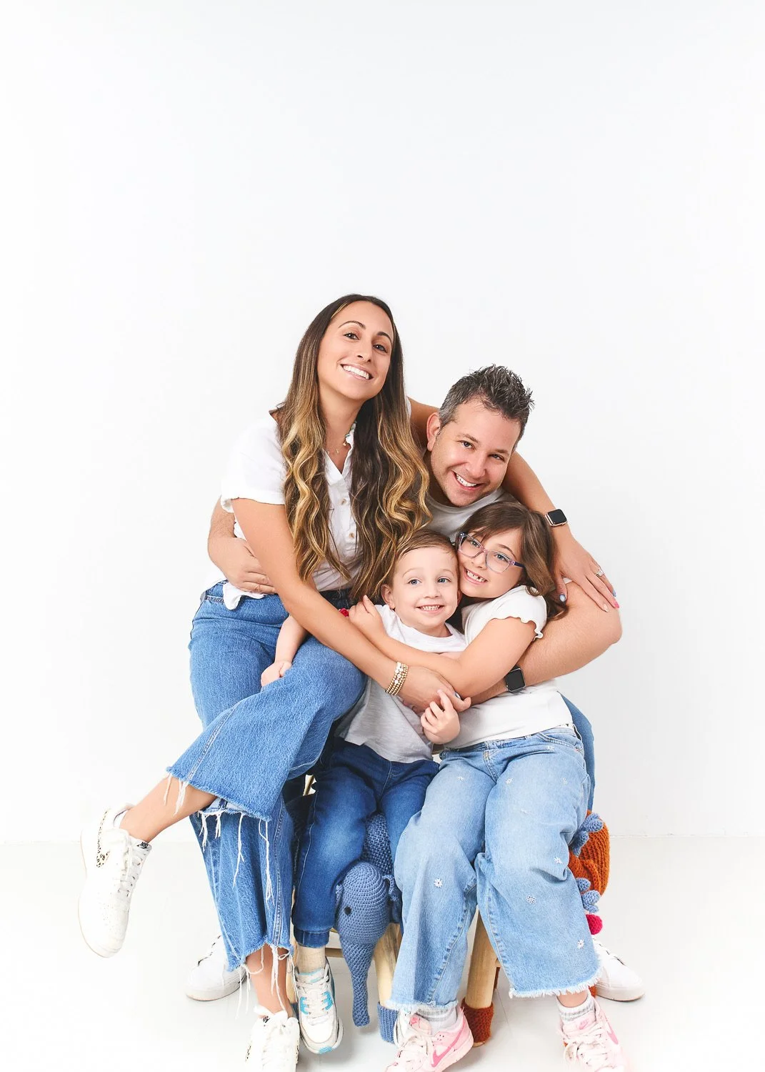 A smiling family of four hugging and posing together against a plain white background.
