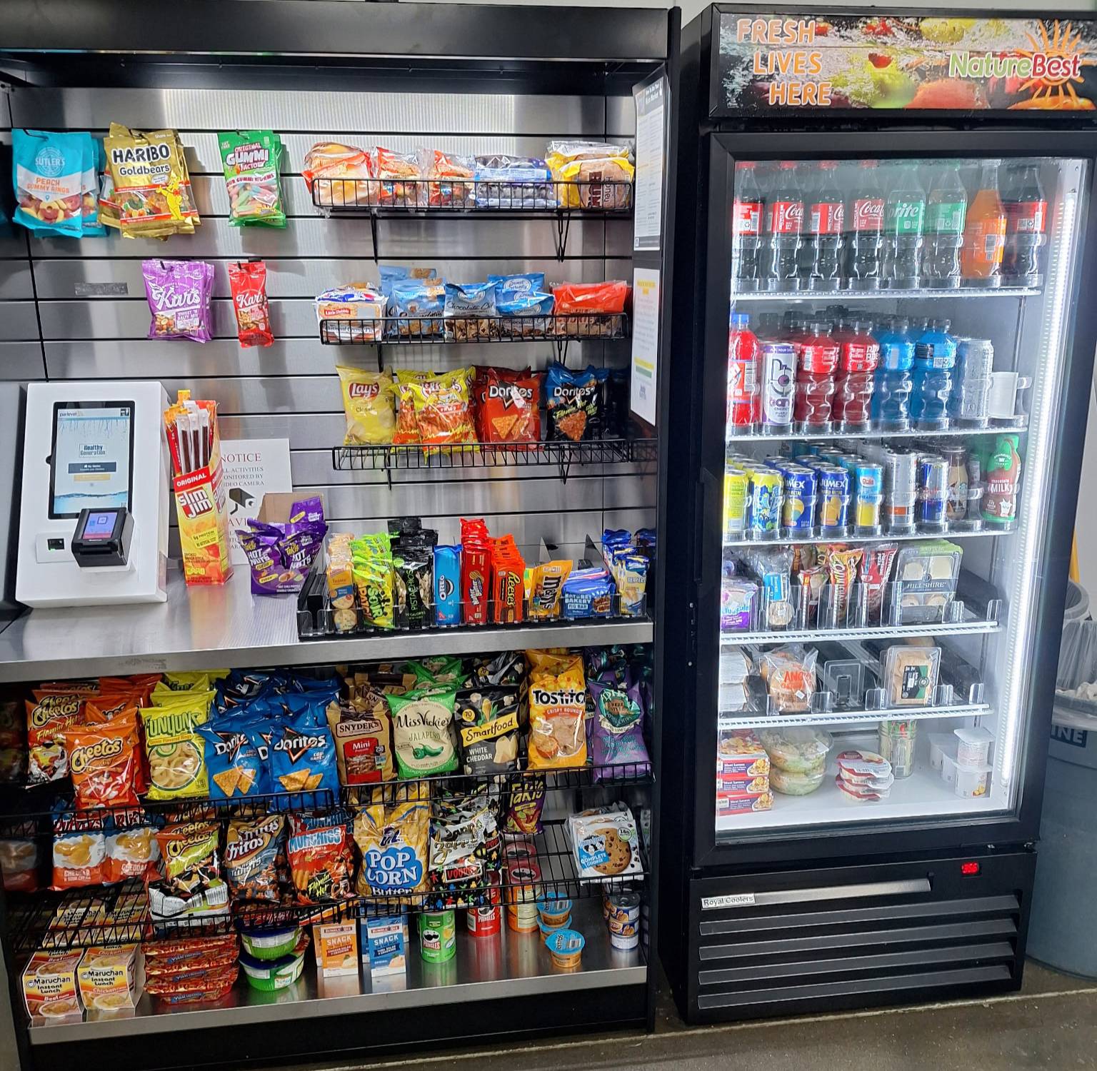 A snack and beverage display with snacks on metal shelves and drinks in a glass-door refrigerator, located in a convenience store or similar setting.