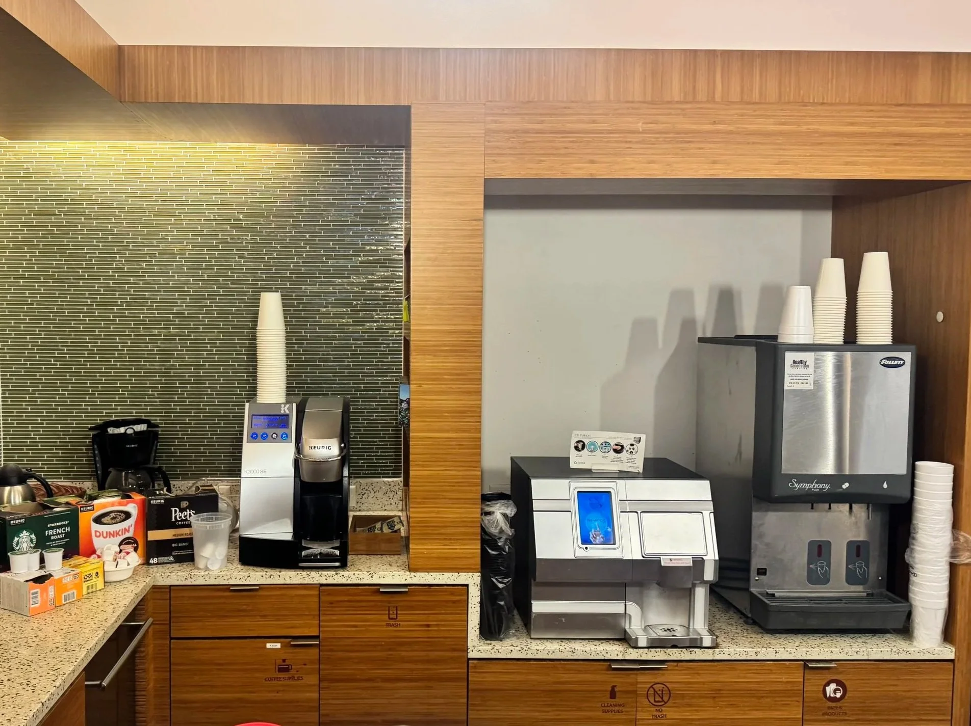 Coffee station with coffee machines, disposable cups, and various supplies in a cafe or break area.