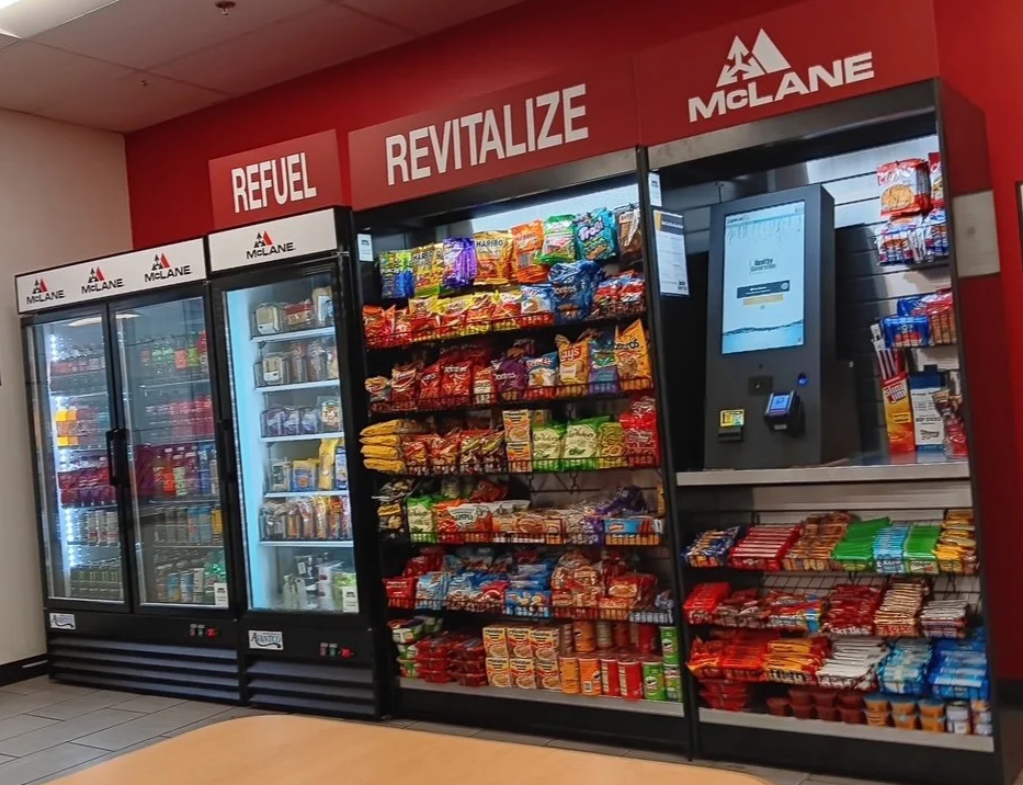 Snack vending machines and a touchscreen ordering kiosk inside a convenience store.