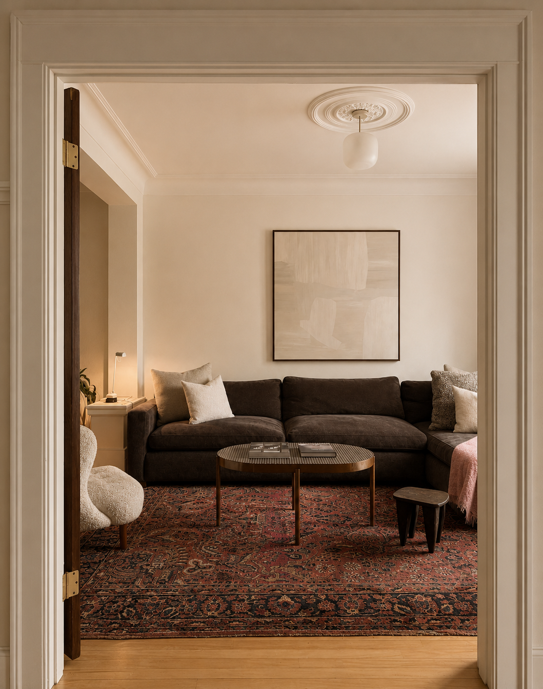 Aménagement d'un salon avec un canapé marron, une table basse, un tapis berbère, un tableau abstrait blanc et beige, et un petit siège.