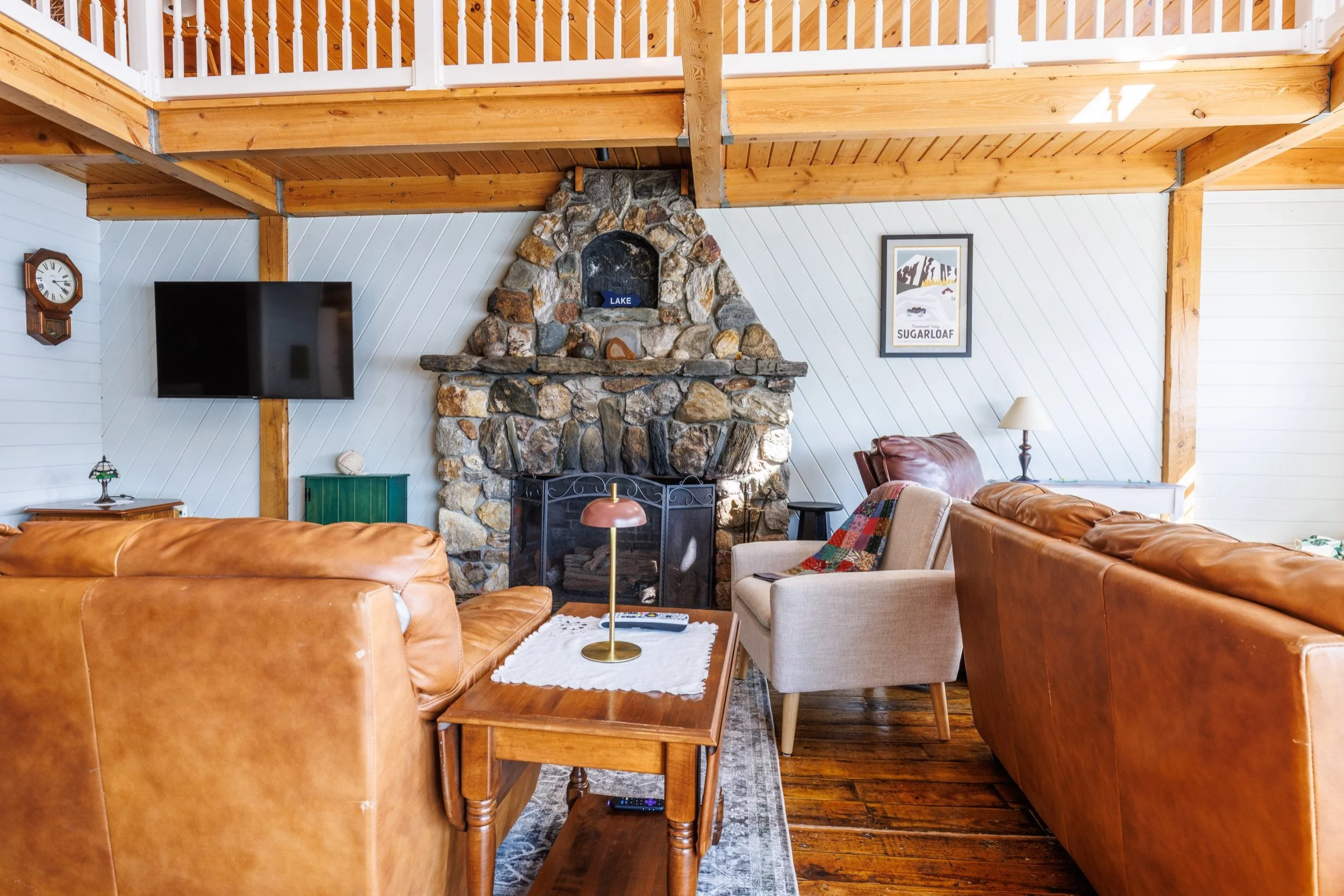 Living room with stone fireplace, leather sofas, a television, wooden furniture, and framed artwork on the wall.
