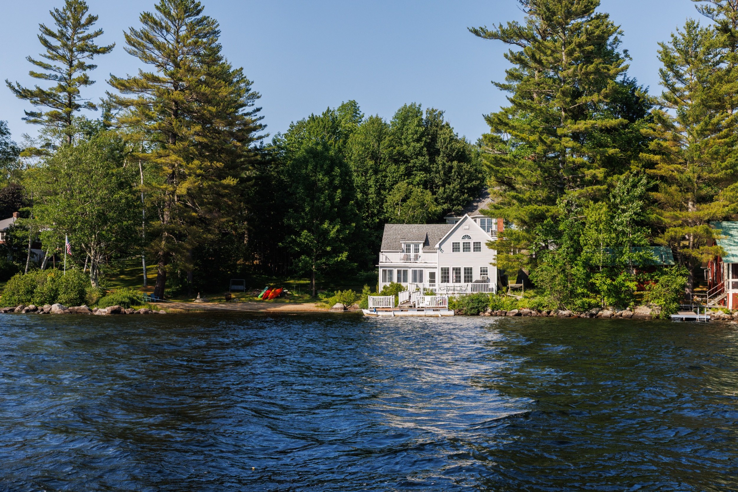 View of houses along a waterbody with trees and blue sky in the background.