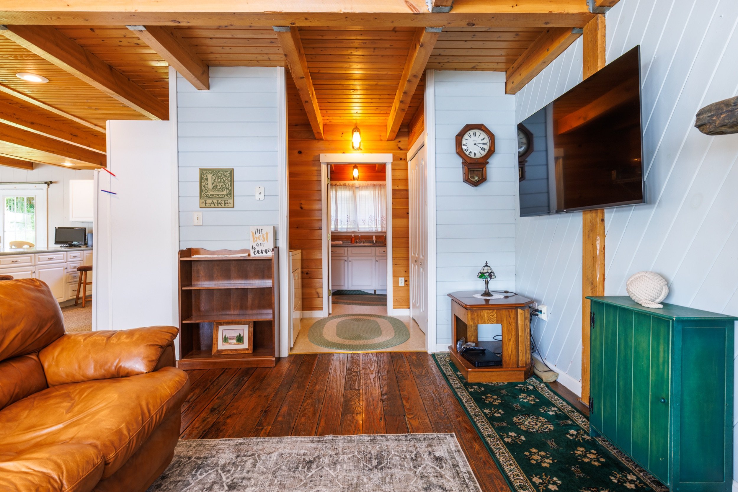 Interior of a cozy cabin living room with wooden ceiling and floor, leather sofa, and wall-mounted flat-screen TV.