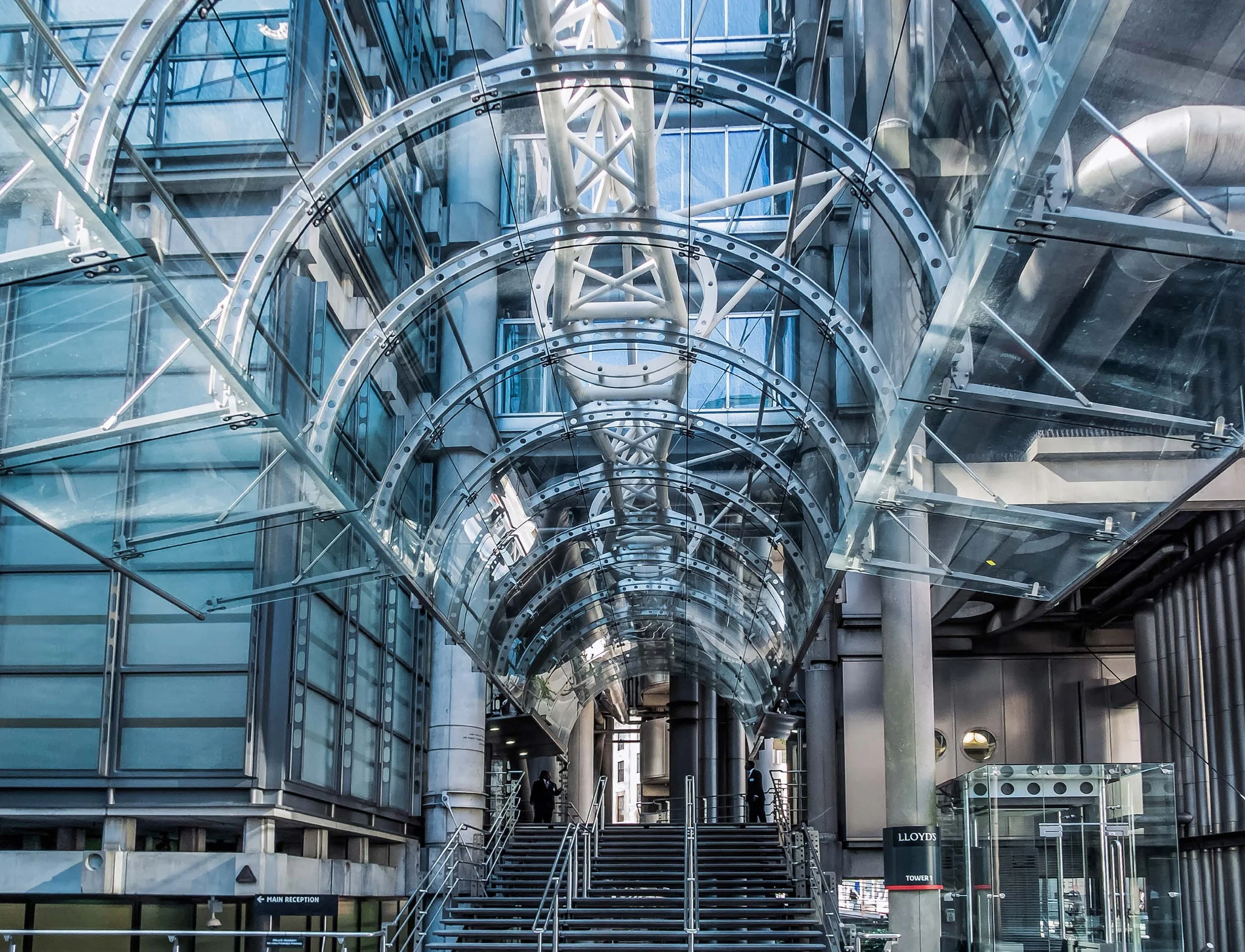 Inside a modern building with glass and steel architecture, multiple levels, escalators, metal spiral structures, and two people walking.