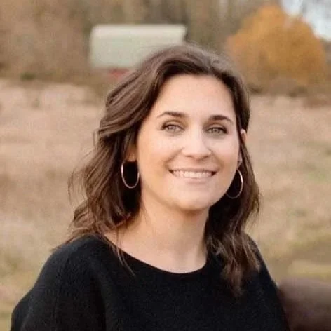 A young woman with wavy brown hair and hoop earrings smiling outdoors in a natural setting - Lead Coordinator, Gordon Duo Weddings