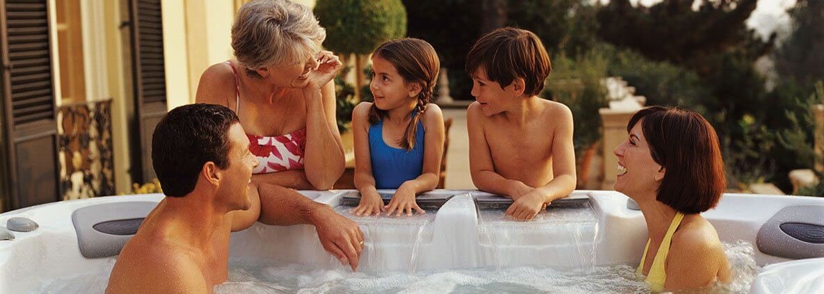Family enjoying time together in Sundance hot tub outside in the evening.