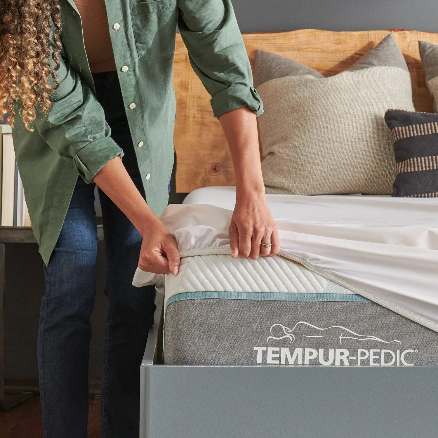 Person adjusting a Tempur-Pedic mattress with a fitted sheet on it.