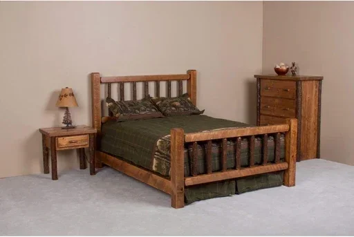 A wooden bedroom set includes a bed with a headboard and footboard, a nightstand with a lamp, and a tall dresser, all placed against plain walls with a light-colored carpeted floor.