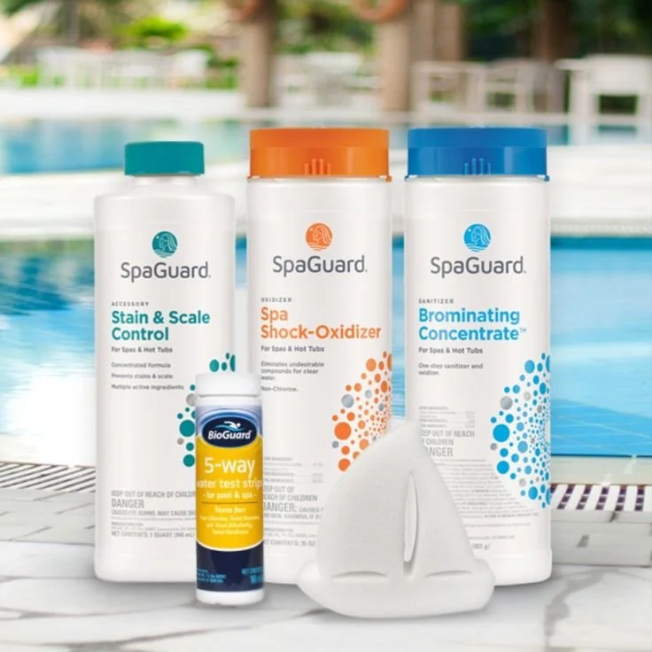 Three bottles of SpaGuard pool chemicals, a small BioGuard test strip, and a white pool alarm float on a marble surface near a swimming pool.