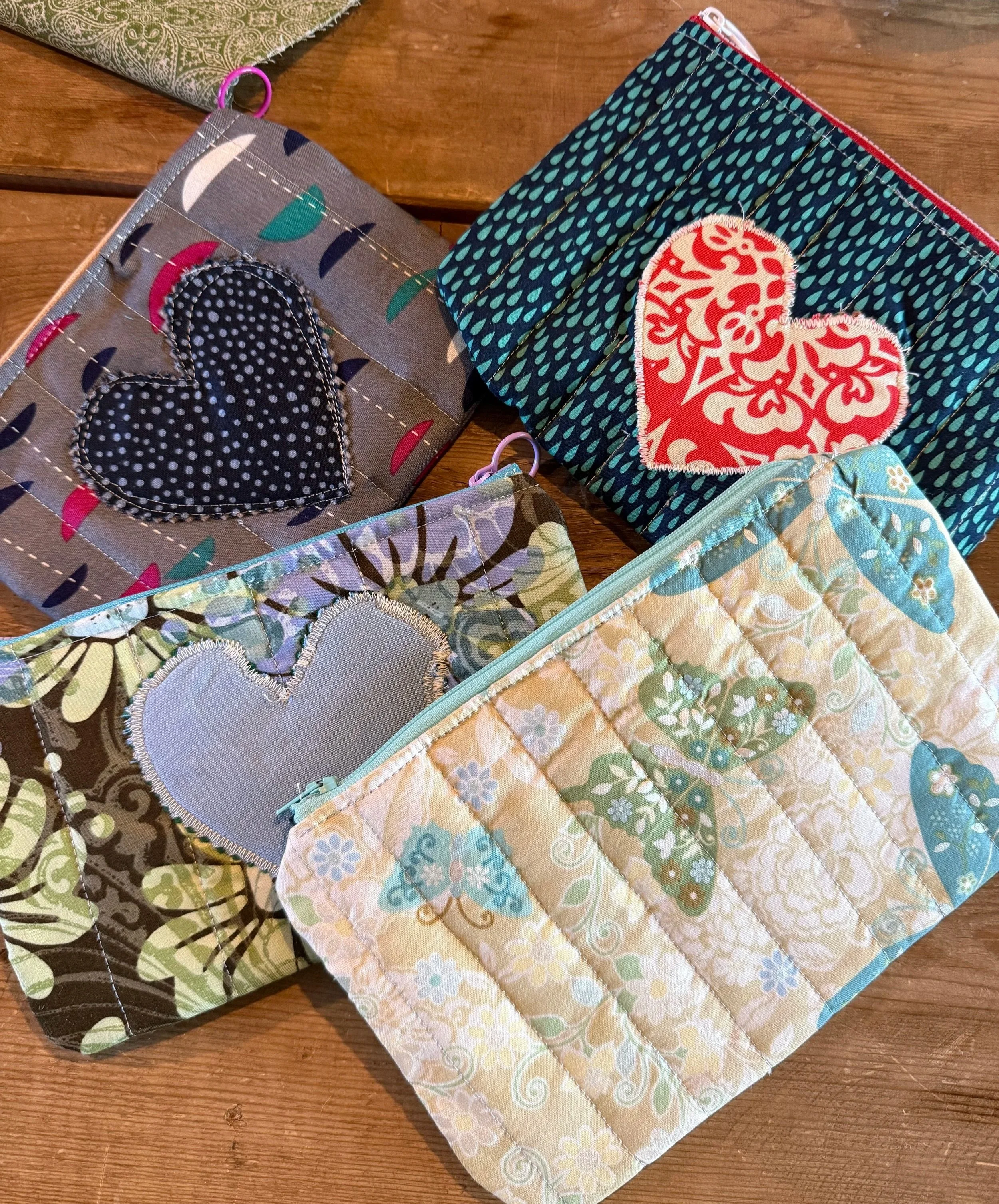 Several quilted fabric pouches with embroidered heart designs, placed on a wooden surface.