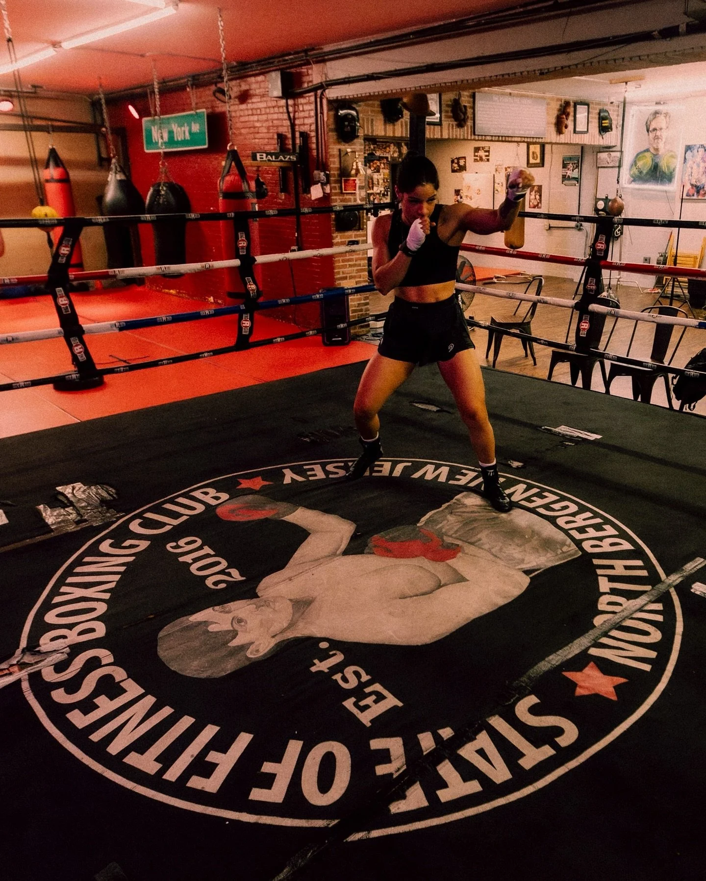 A female boxer practicing in a boxing gym with punching bags and boxing equipment in the background.