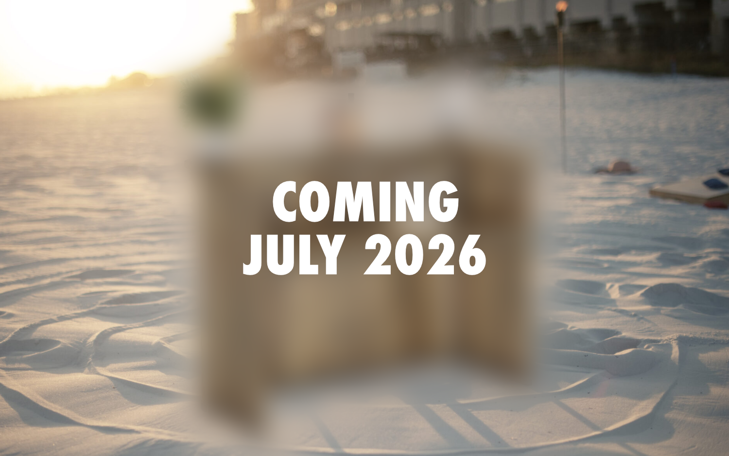 A beach scene at sunset with a blurred portable bar in the foreground. The text 'Coming July 2026' is overlaid on the image.