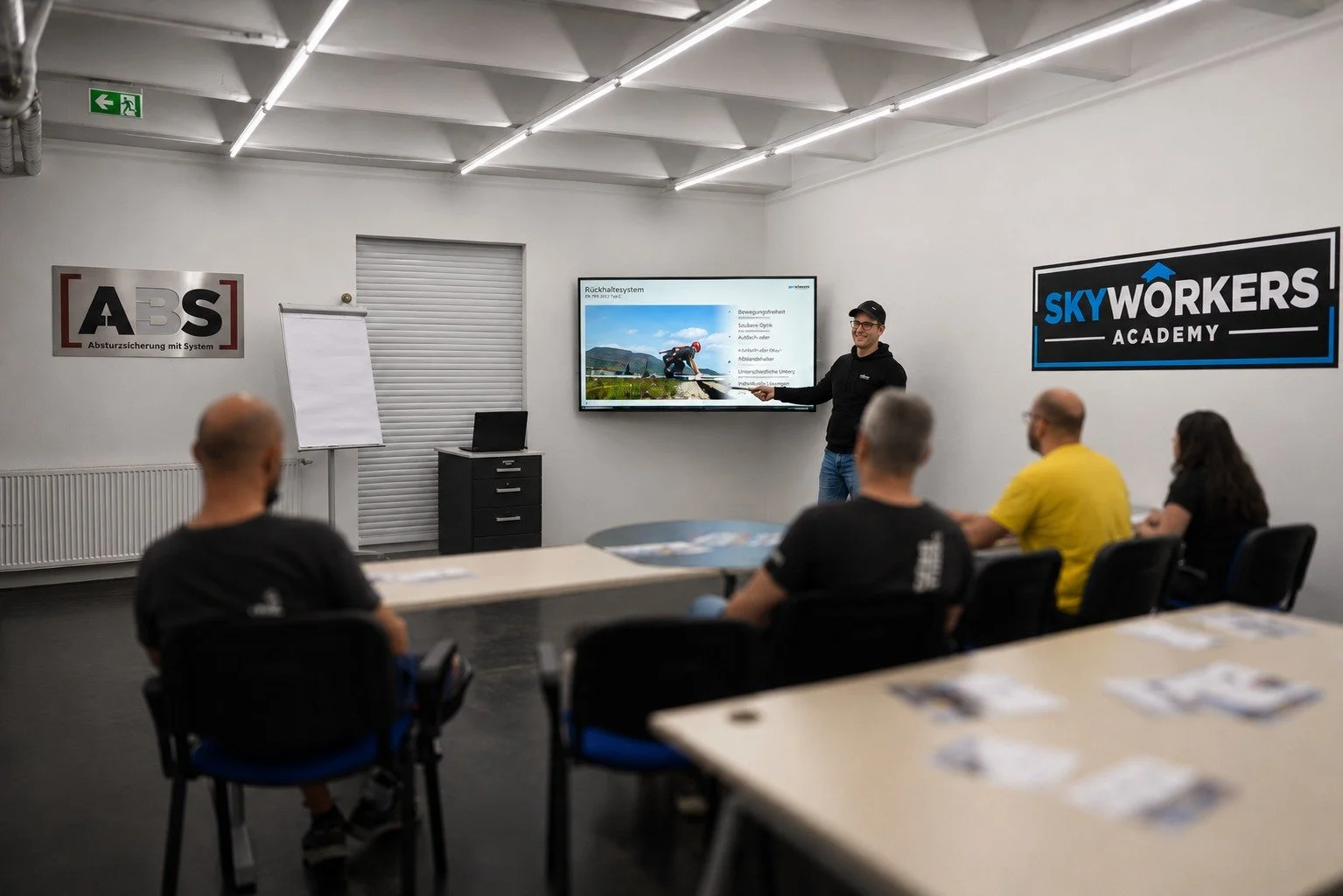 Moderner Schulungsraum der Skyworkers Academy während einer praxisnahen ABS-Schulung. Ein Ausbilder vermittelt theoretische Inhalte anhand einer Präsentation und bereitet die Teilnehmer auf sicheres Arbeiten in der Höhe vor.