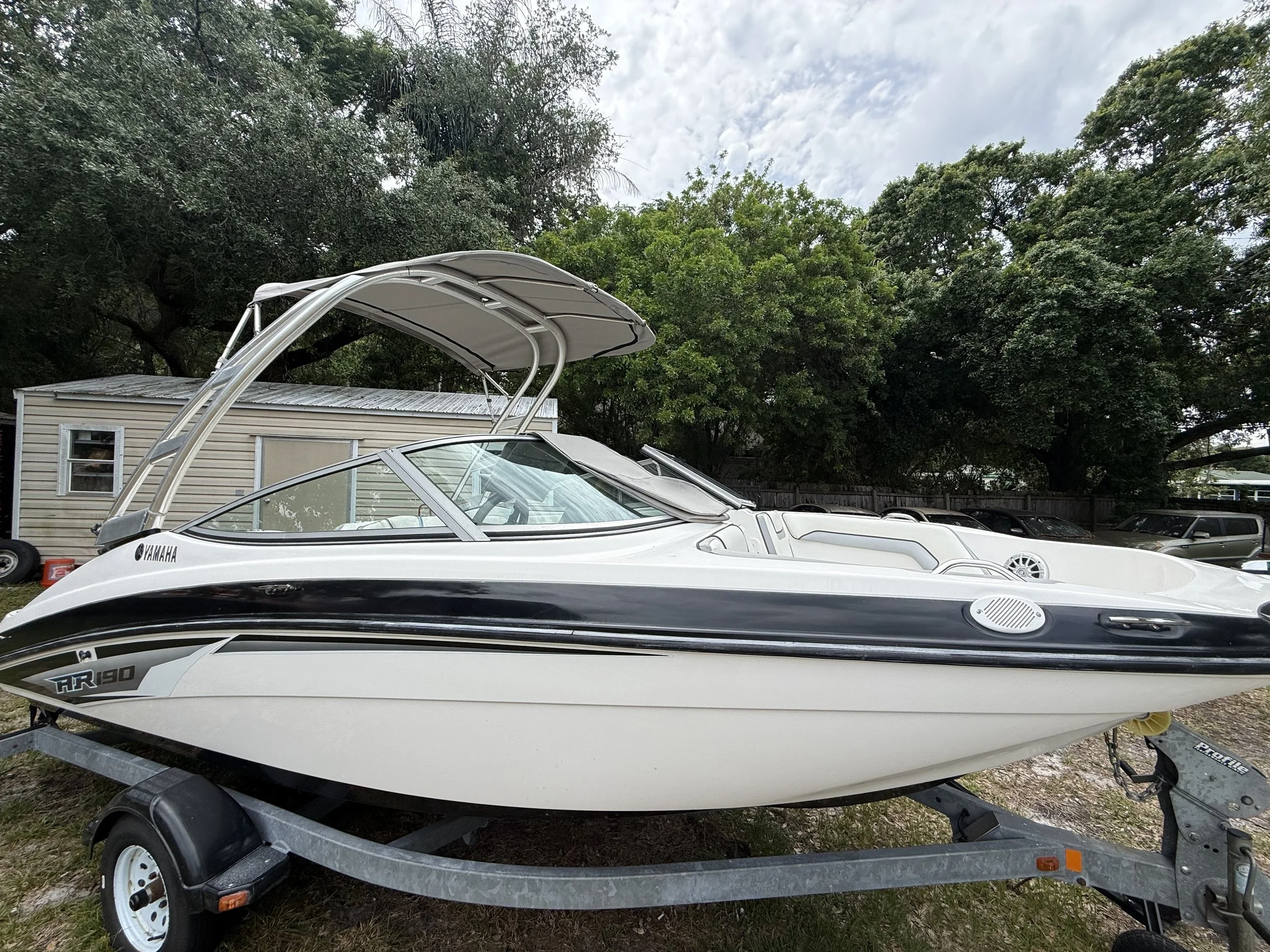 A Yamaha AR 190 speedboat on a trailer, parked outdoors near trees and a small building.