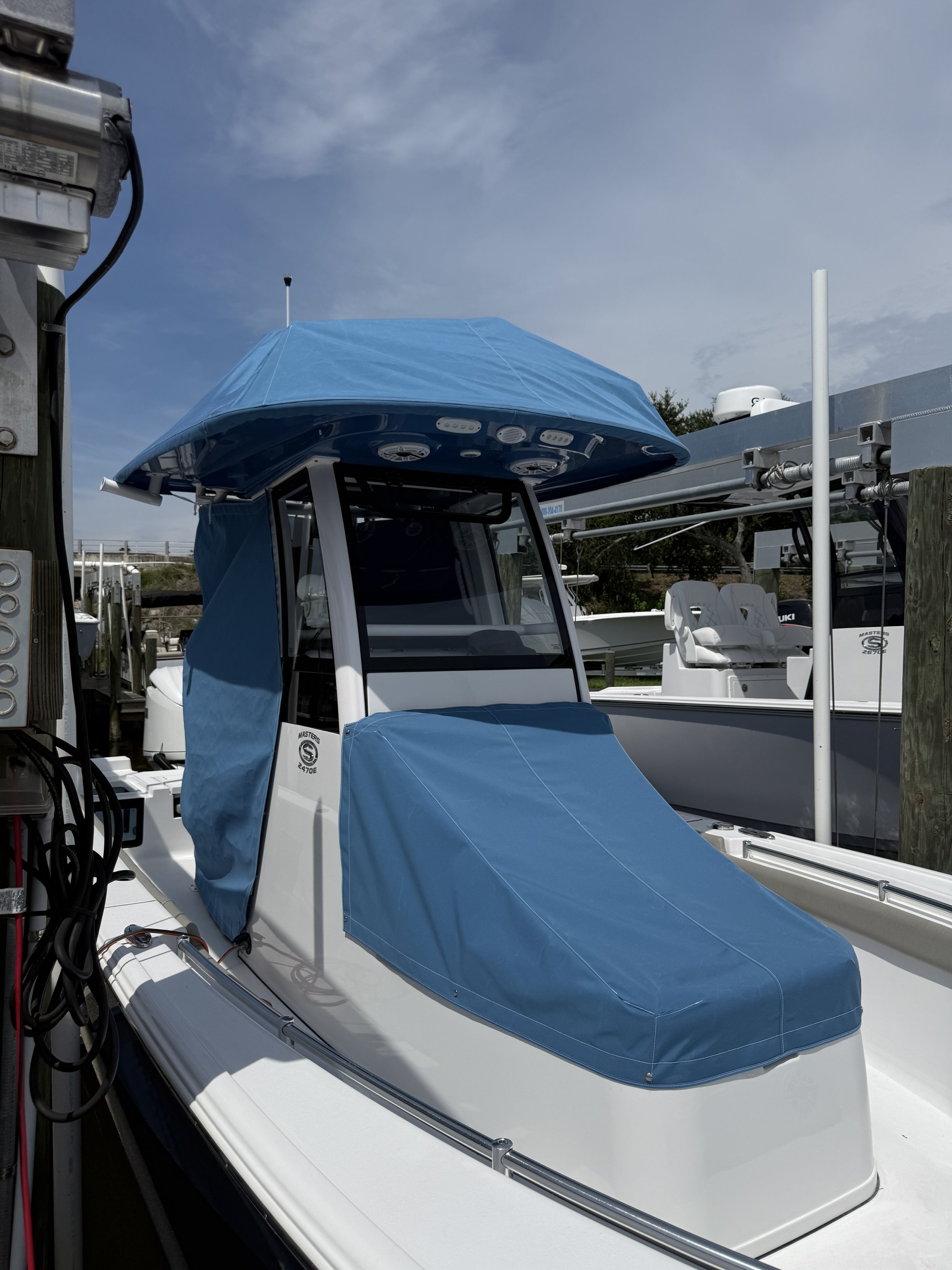 A boat with a blue cover, docked at a marina, with other boats and cloudy sky in the background.
