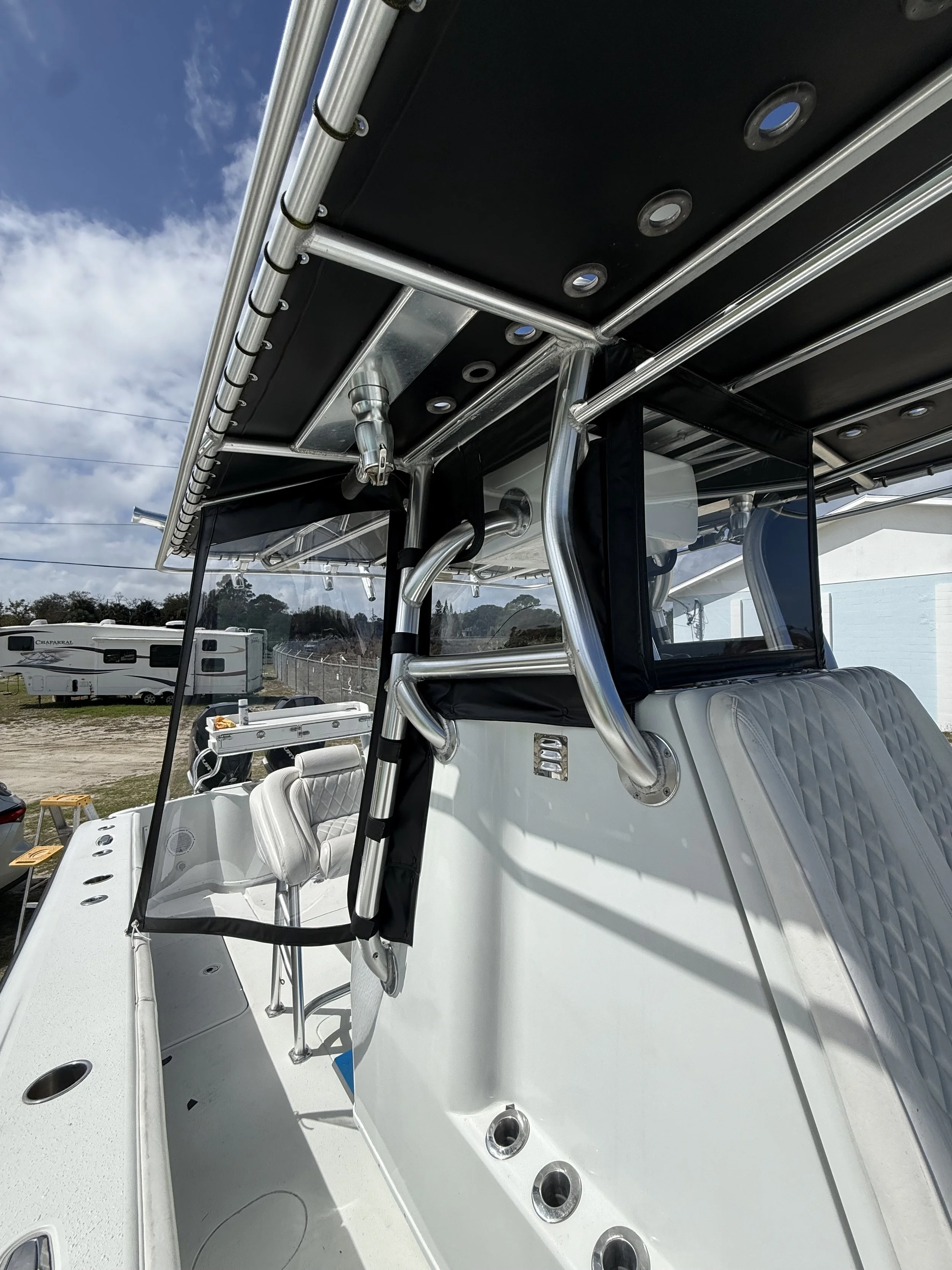 A view of a pontoon boat's upper deck, with metal railings, cup holders, and cushioned seats in front of a fence, under a partly cloudy sky.