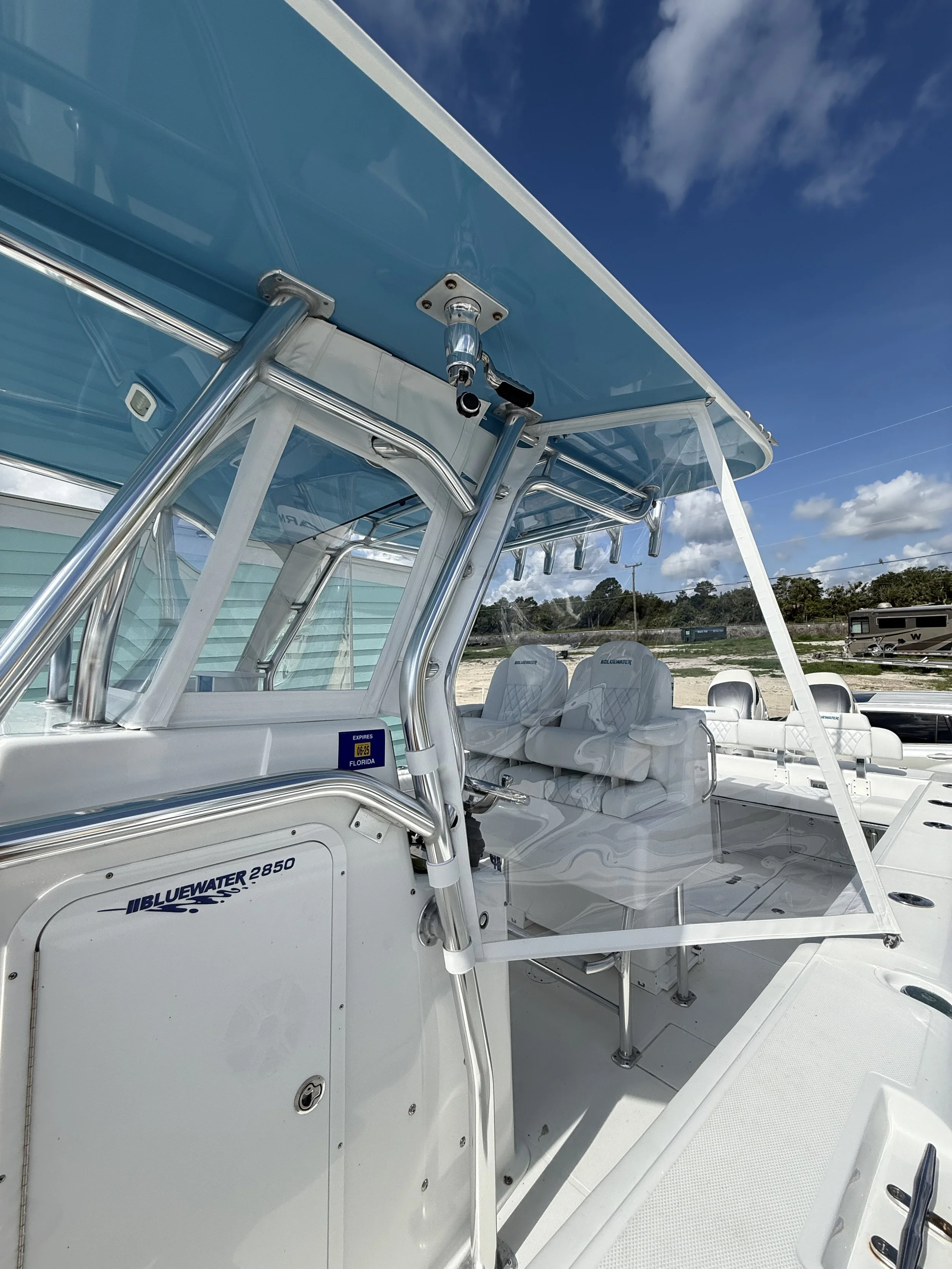 A white Bluewater 2850 boat with a hardtop roof, seating area, and a fish rod holder, parked outdoors on a sunny day with a blue sky and some clouds.