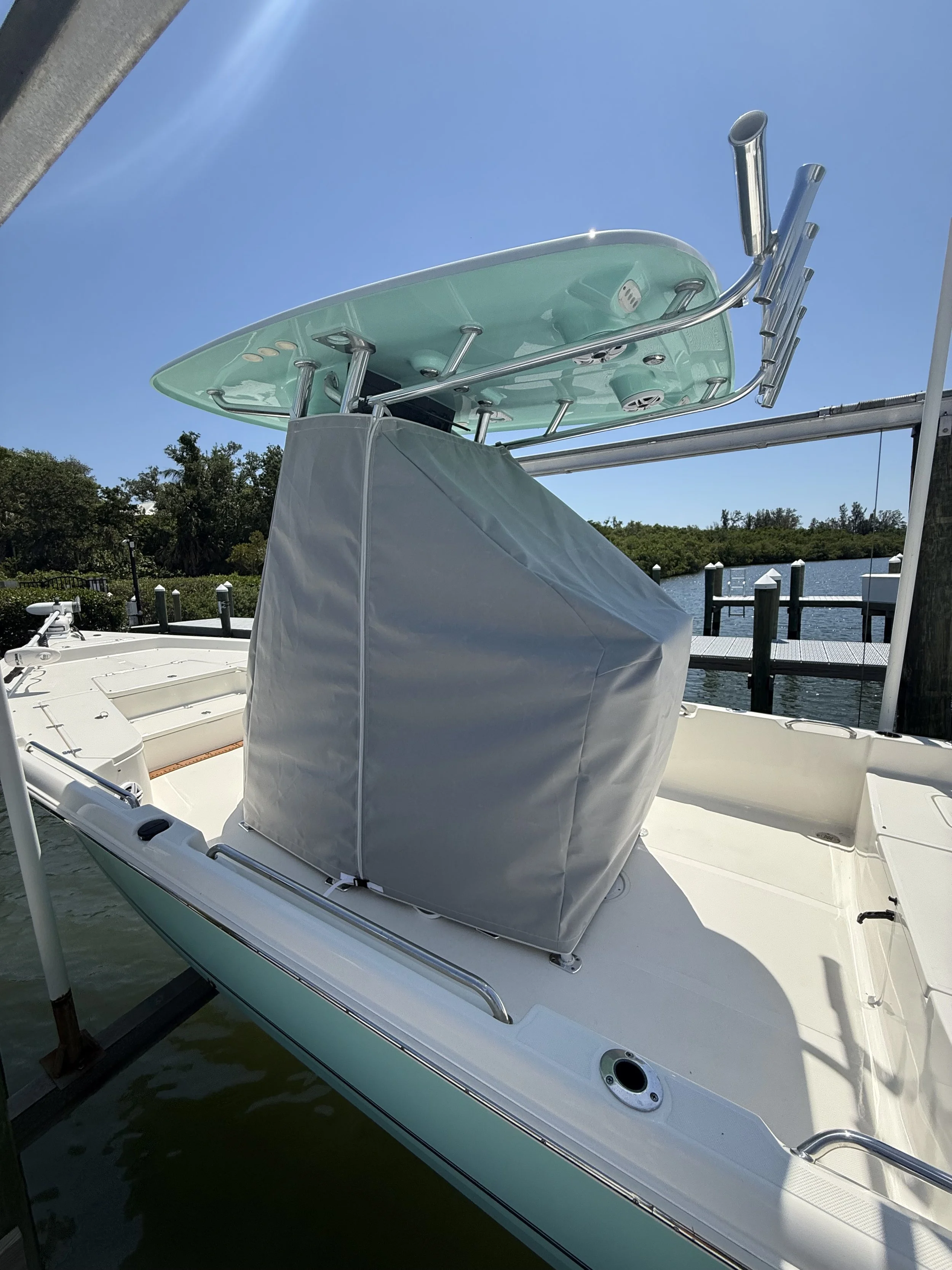 A boat docked at a marina with a canopy, water, and trees visible in the background under a clear blue sky.