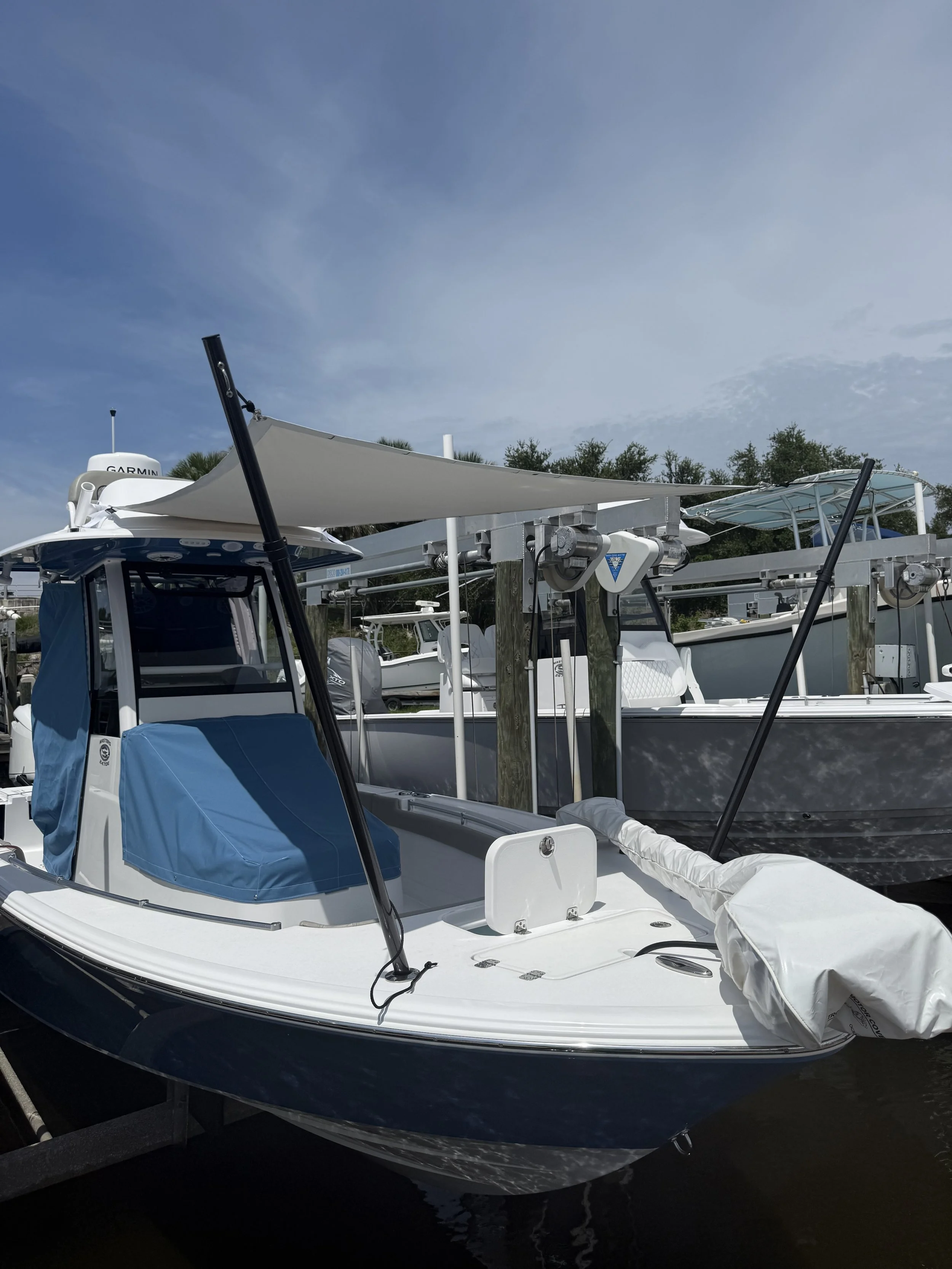 A white and black motorboat docked at a marina, with an awning, covered equipment, and other boats in the background.