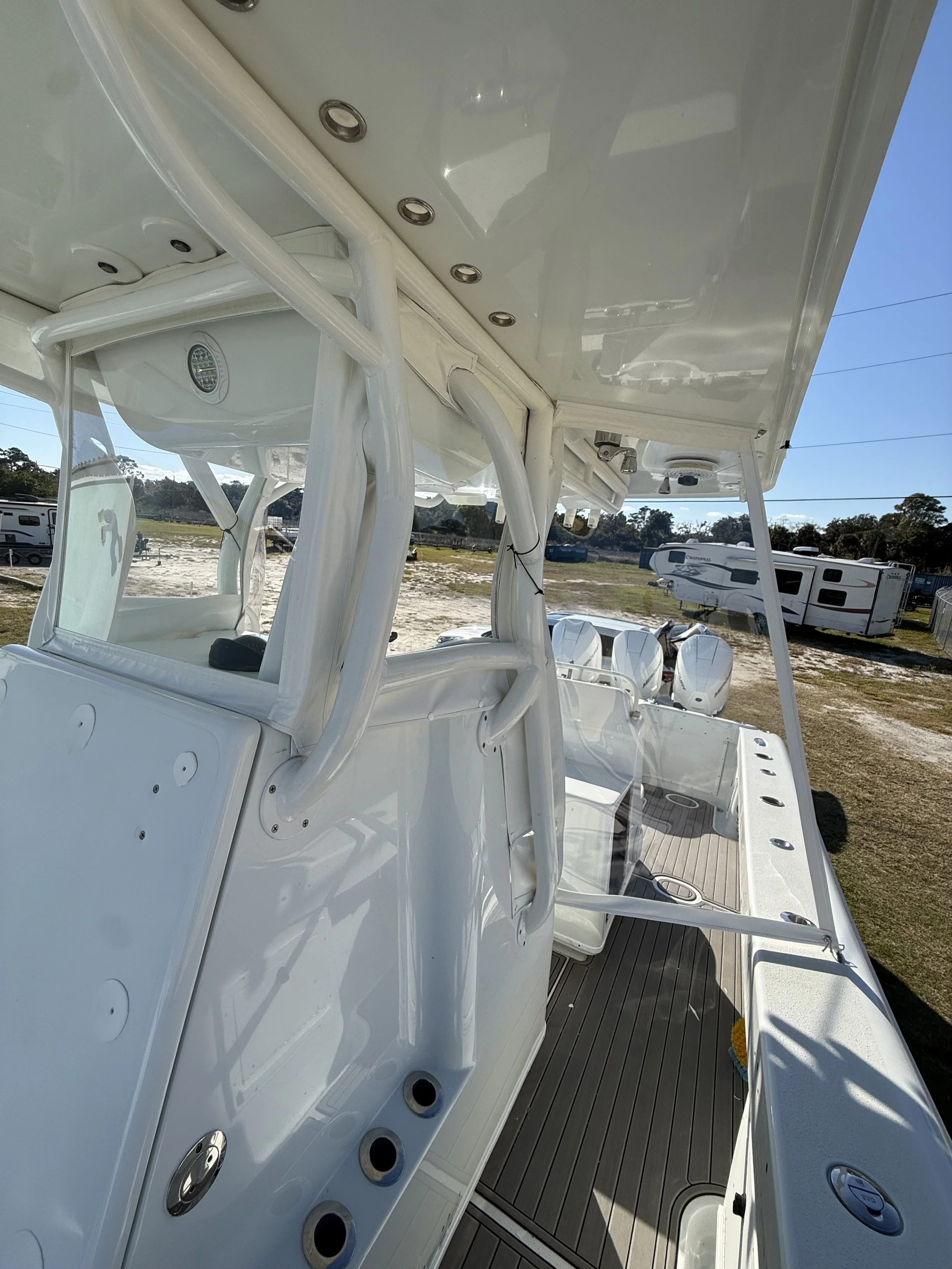 The image shows the interior of a white motorboat with built-in seating, several speakers, and a wooden deck floor, with other RVs and trailers in the background under a clear sky.
