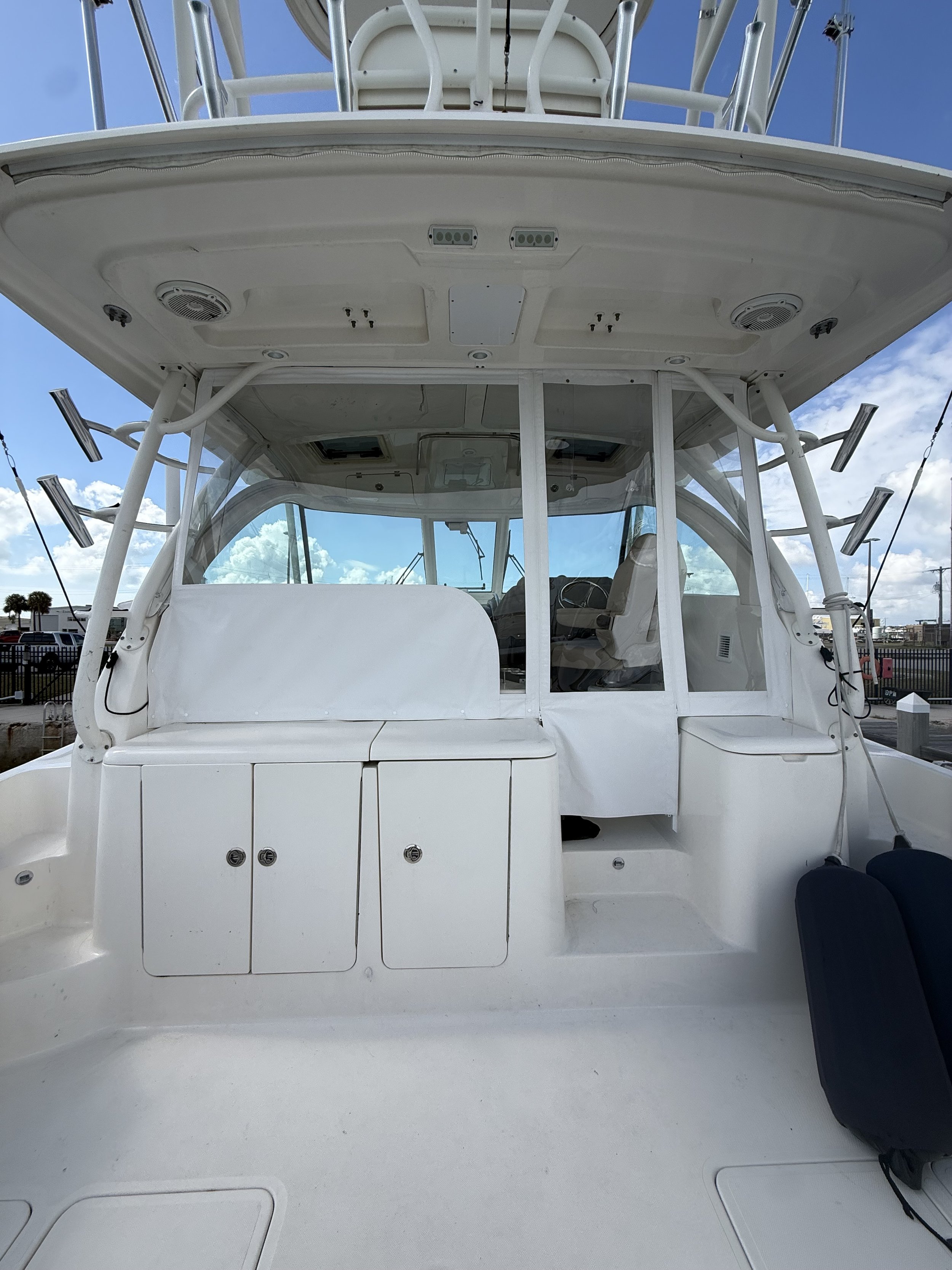 View from inside the cabin of a white boat, looking forward, with a clear blue sky and some clouds visible in the background.