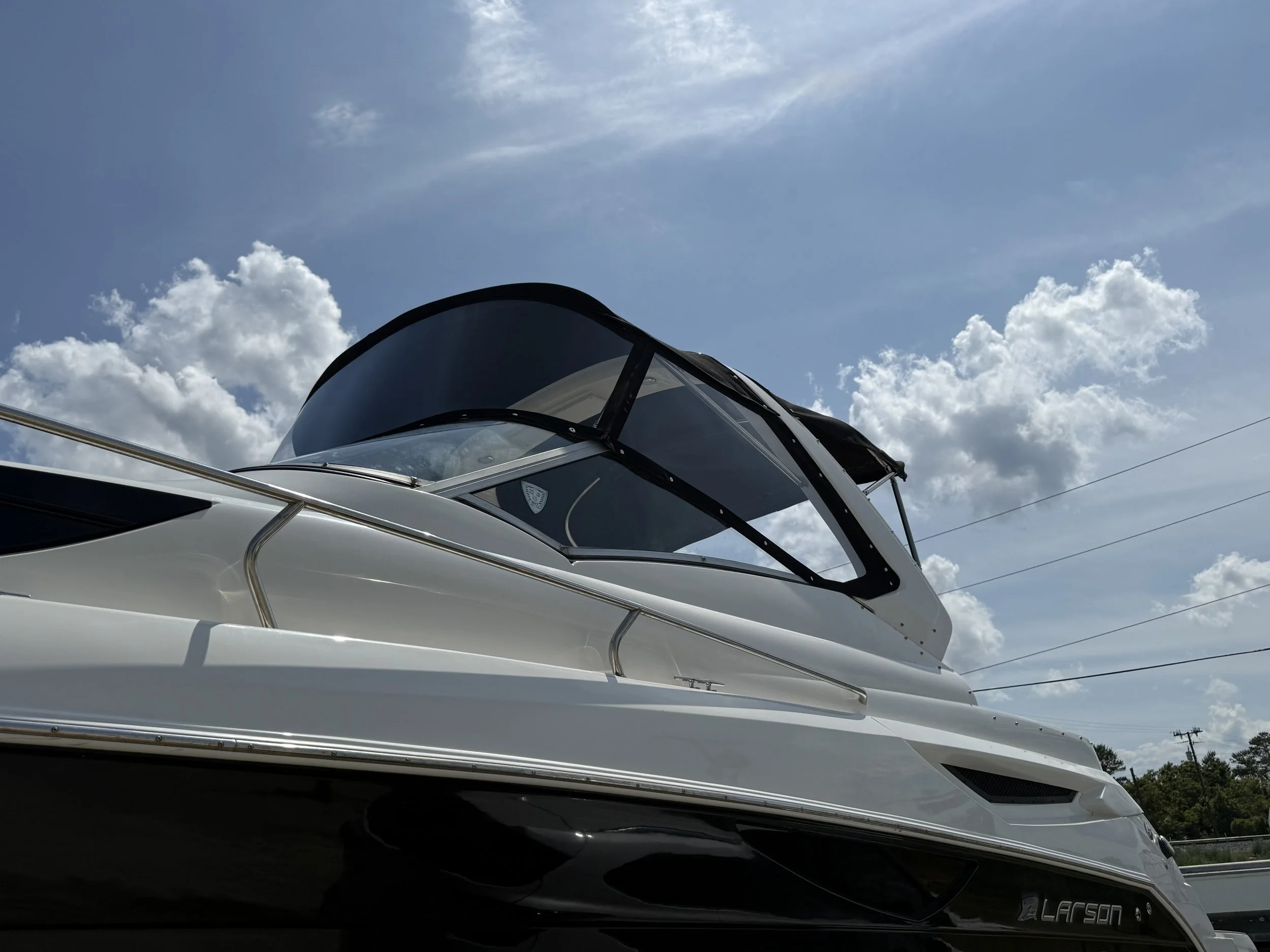 Close-up of a white yacht boat with black accents, focused on the front part with a curved window, against a background of a partly cloudy sky.