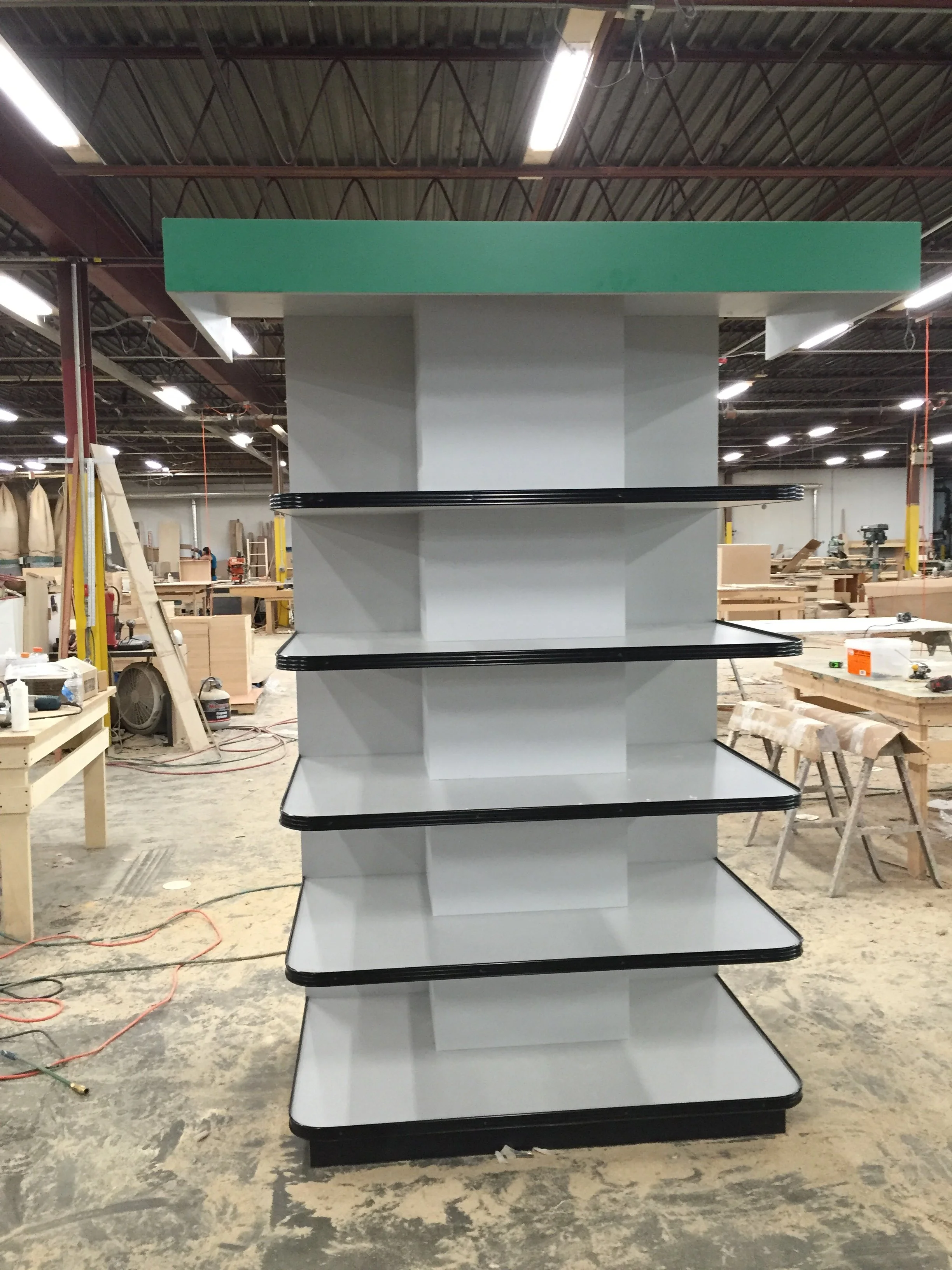 A retail display shelf with four empty black-trimmed white shelves in an industrial warehouse setting.