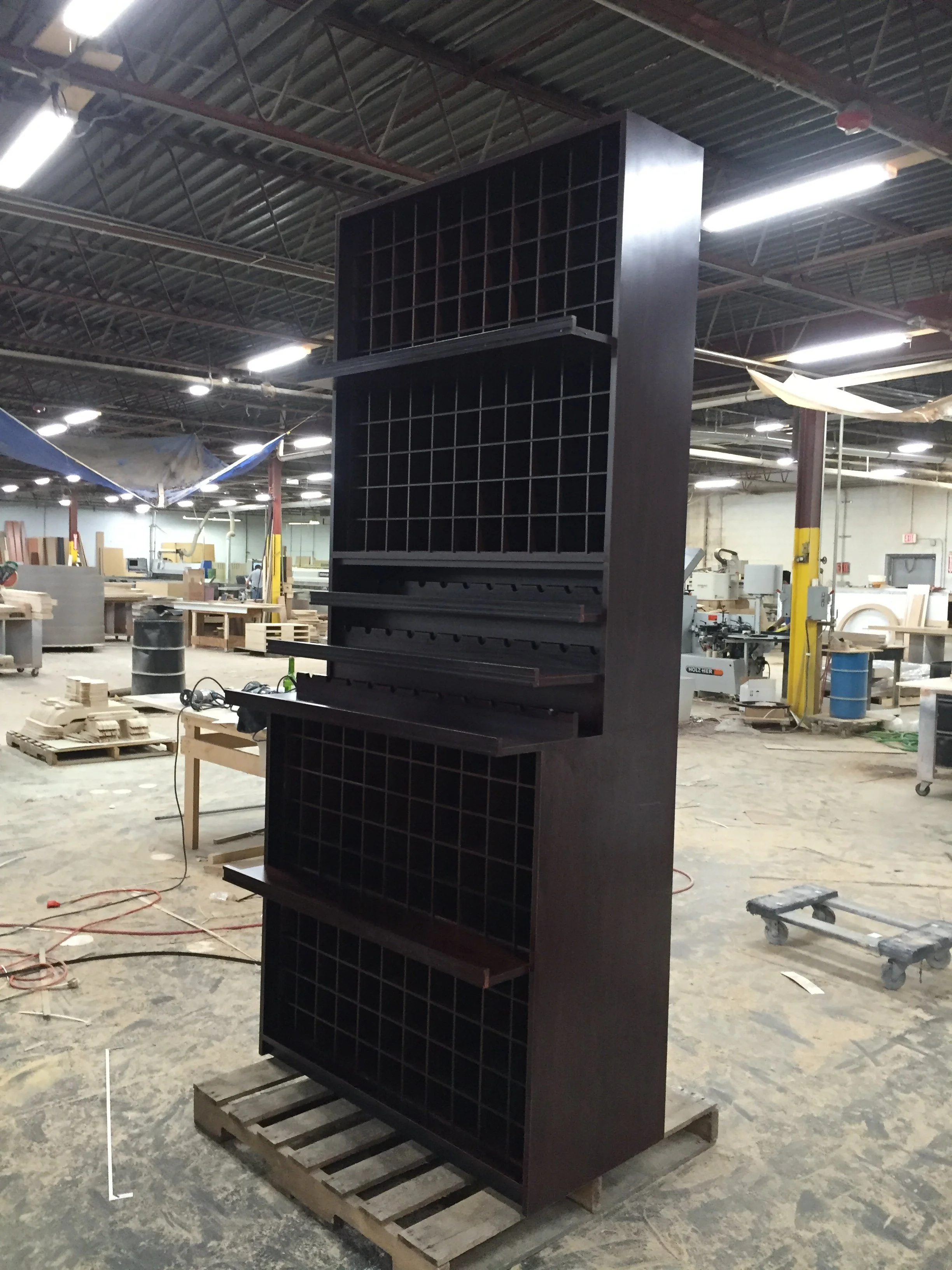 A tall black shelving unit with multiple square compartments in an industrial workshop with tools, wood, and equipment visible in the background.