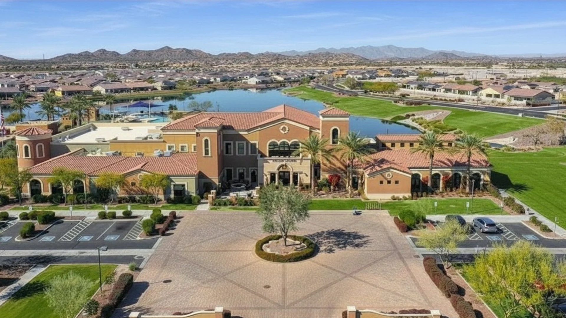 Aerial view of the Village Center clubhouse at CantaMia at Estrella overlooking community lakes with the Estrella Mountains in the background.