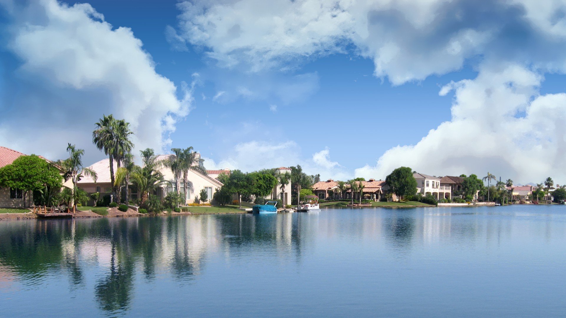 A scenic view of houses along a waterway with boats, lush green trees, palm trees, and a partly cloudy sky.