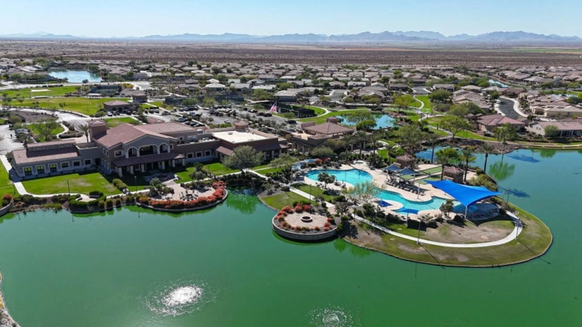 Aerial view of the Village Center clubhouse, resort-style pool, and lakes at CantaMia at Estrella, a 55+ community in Goodyear, Arizona.