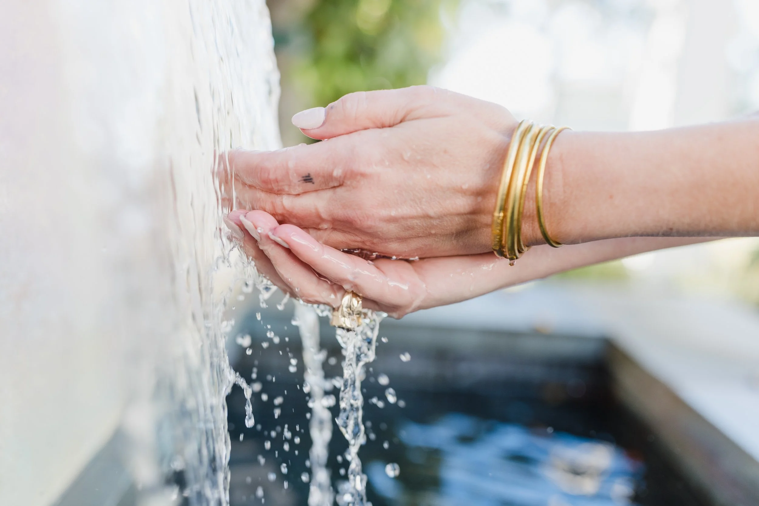 Close-up of a person's hand with jewelry, fingers touching a flowing stream of water.