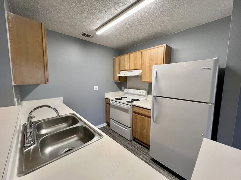 Kitchen with gray walls, wooden cabinets, white refrigerator, stove, and stainless steel sink.