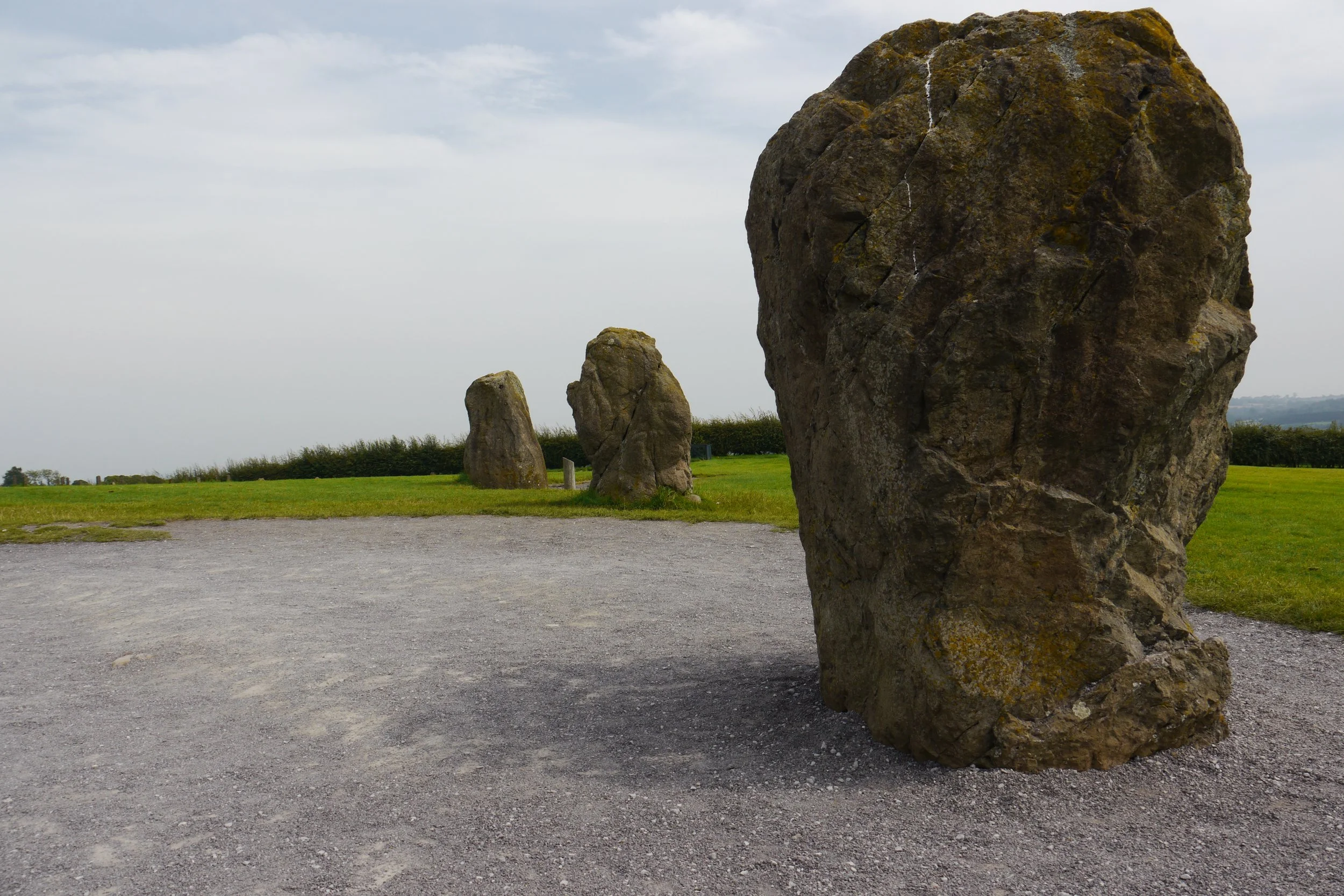 Large standing stone with a smaller stone nearby on a grassy field with a cloudy sky.