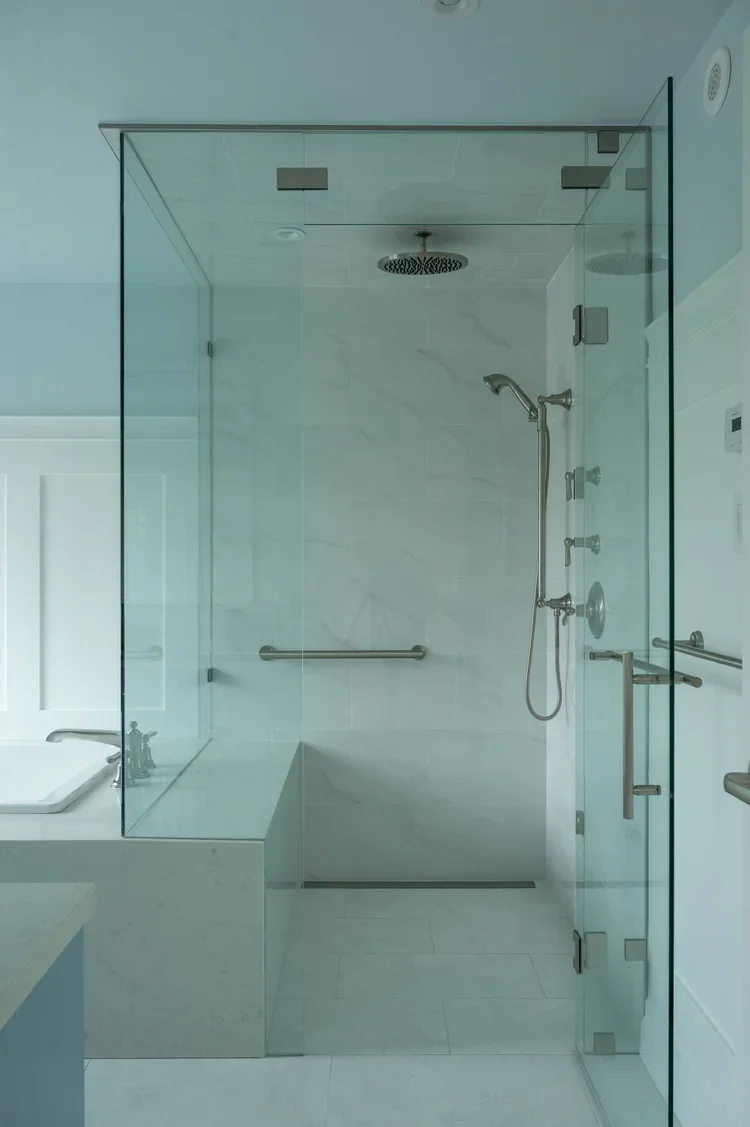 Clean, modern glass-enclosed walk-in shower with a rainfall showerhead and a handheld shower, featuring a towel bar and grab bars on the wall.