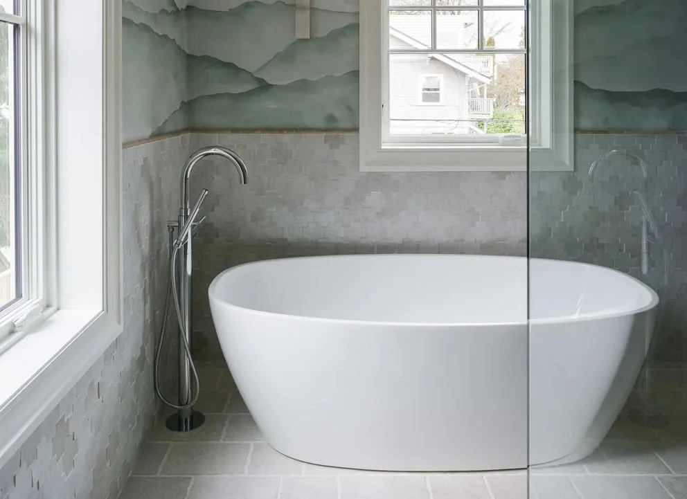 Modern bathroom with a freestanding white bathtub, surrounded by textured tile walls, with a window showing an outdoor view.