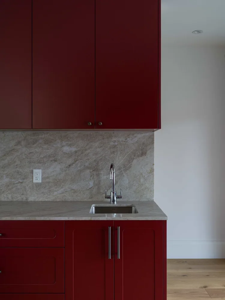 Kitchen with red cabinets, marble backsplash, stainless steel sink, and faucet.