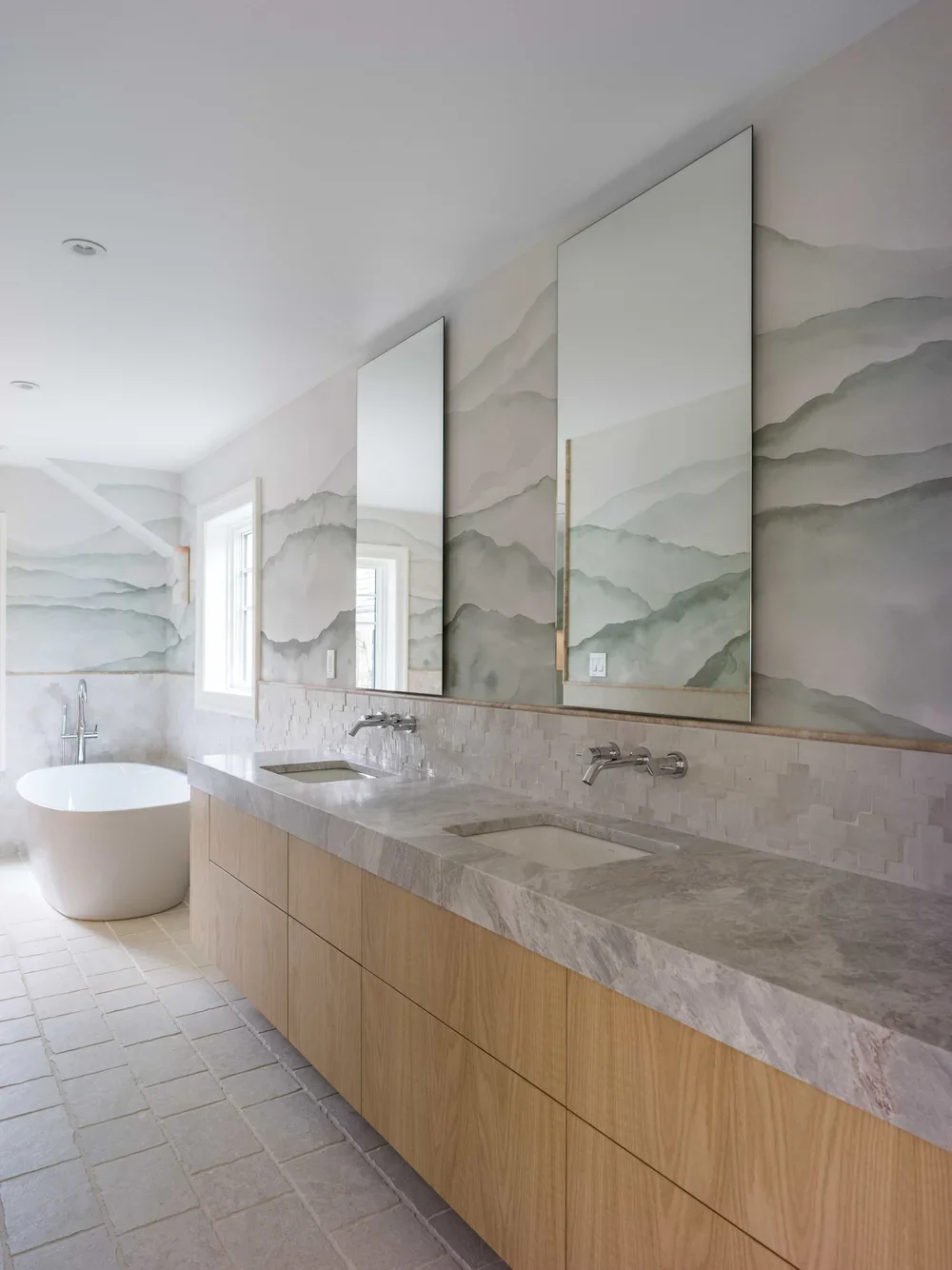 Modern bathroom with double vanity, marble countertop, two rectangular sinks, large mirrors, watercolor mountain wall art, bathtub near window, tiled floor, natural light.