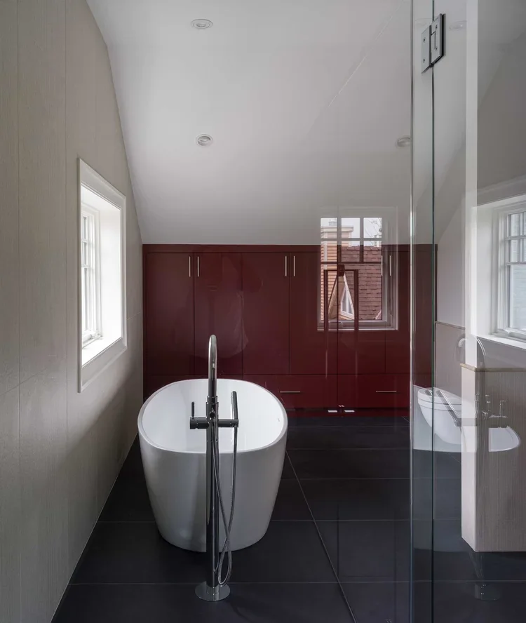 Modern bathroom with a white freestanding bathtub, dark wooden cabinets, and two small windows letting in natural light.