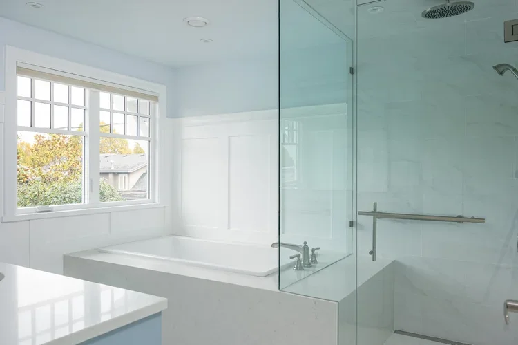 Bright bathroom with a large bathtub under a window, and a glass-enclosed shower area with a grab bar.