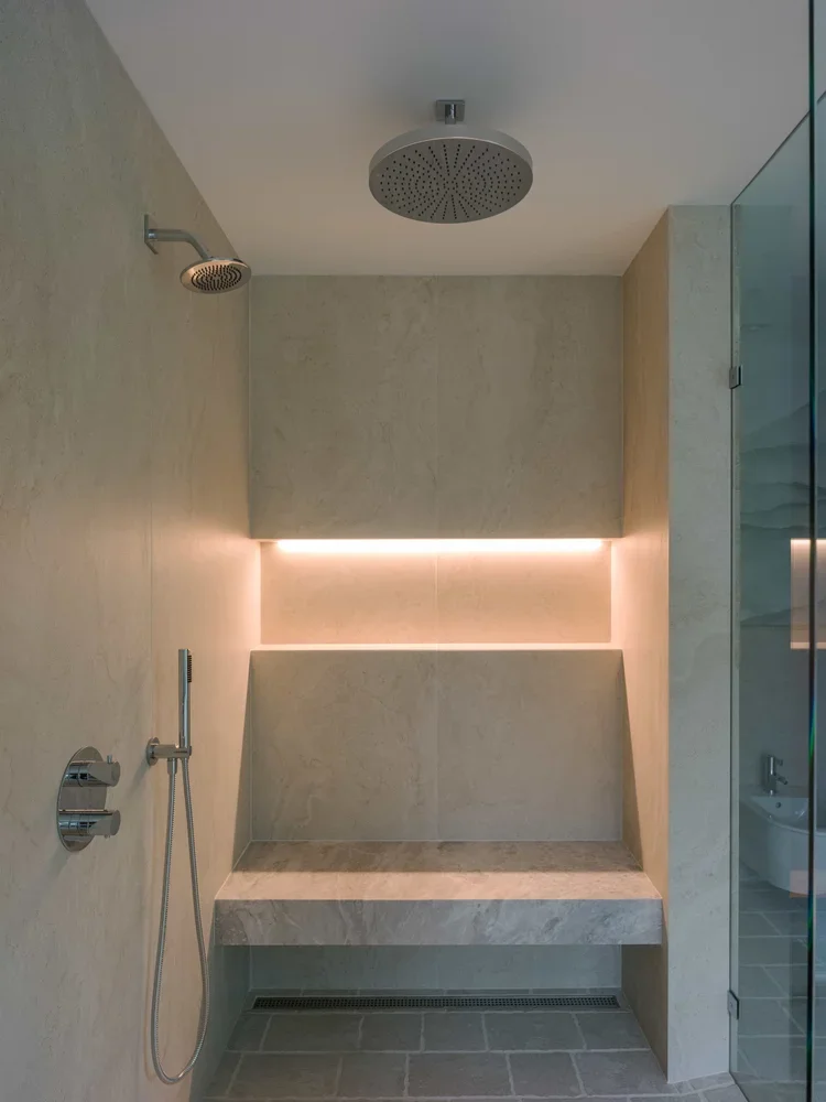 Modern shower area with a large overhead rain shower, a smaller showerhead, a built-in bench with LED lighting, and a handheld shower attachment.