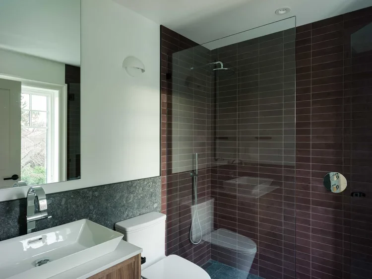 Modern bathroom with a walk-in shower with dark red tiles, a white toilet, and a sink with a mirror