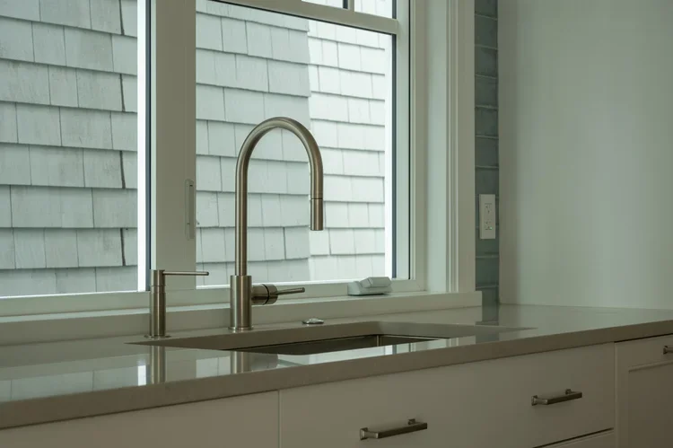 Kitchen sink with a modern faucet in front of a large window showing an exterior wall with white siding.