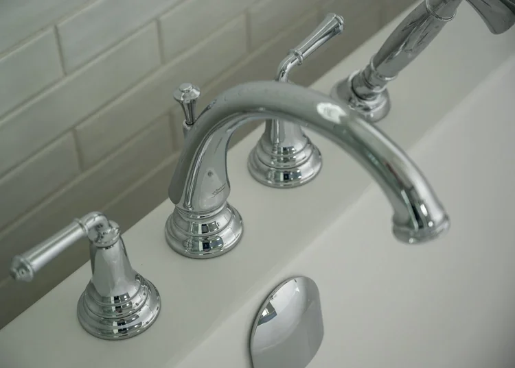 Close-up of a shiny chrome bathroom faucet and handles mounted on a white bathtub.