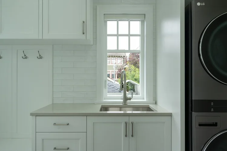 Clean kitchen with white cabinets, a window above the sink, and a black stacked washer and dryer on the right.