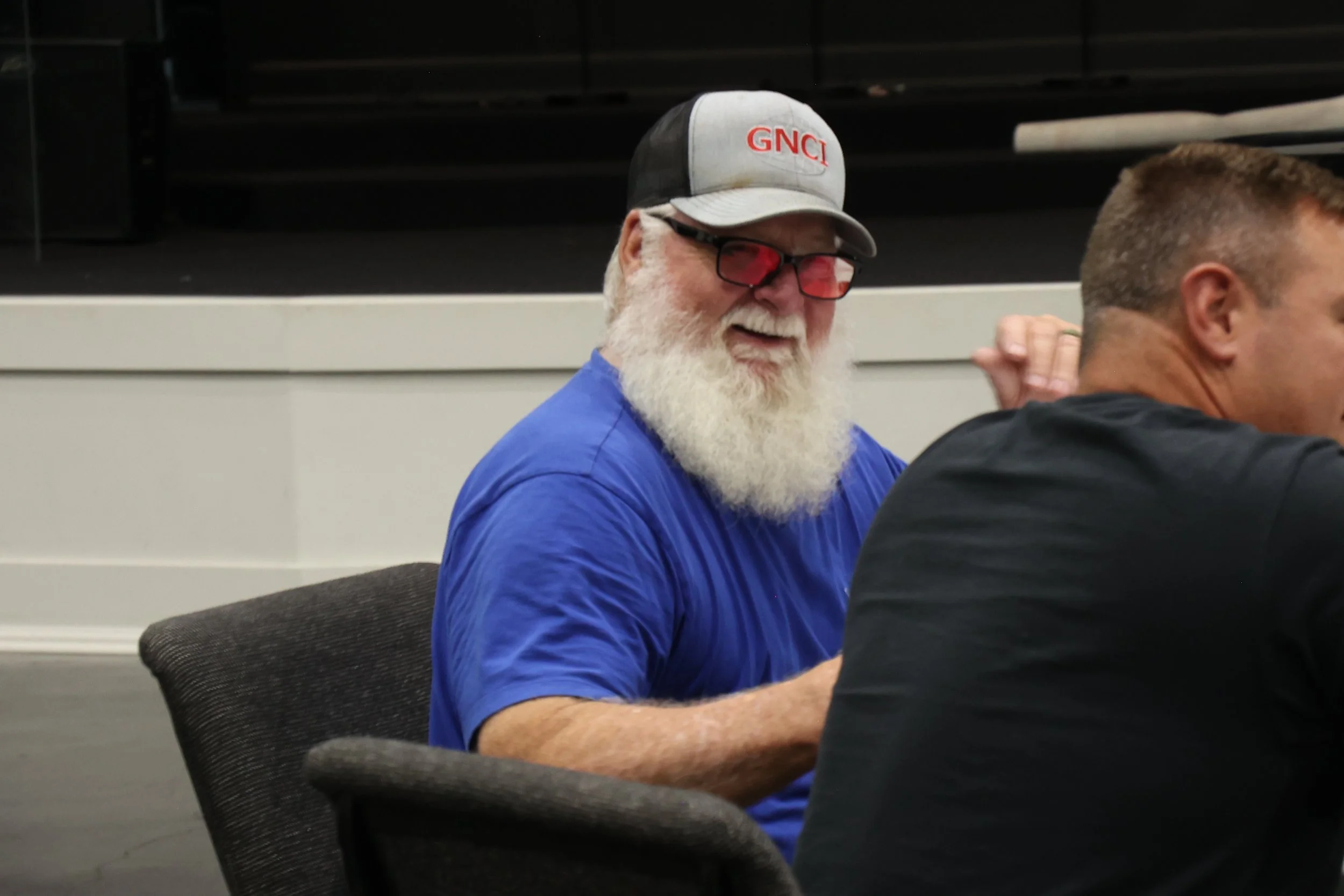 Older man with a white beard and glasses engaged in conversation with another man