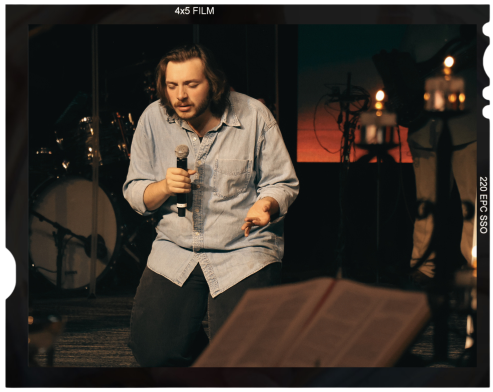 Picture of a young man on his knees with eyes closed holding a mic and worshiping