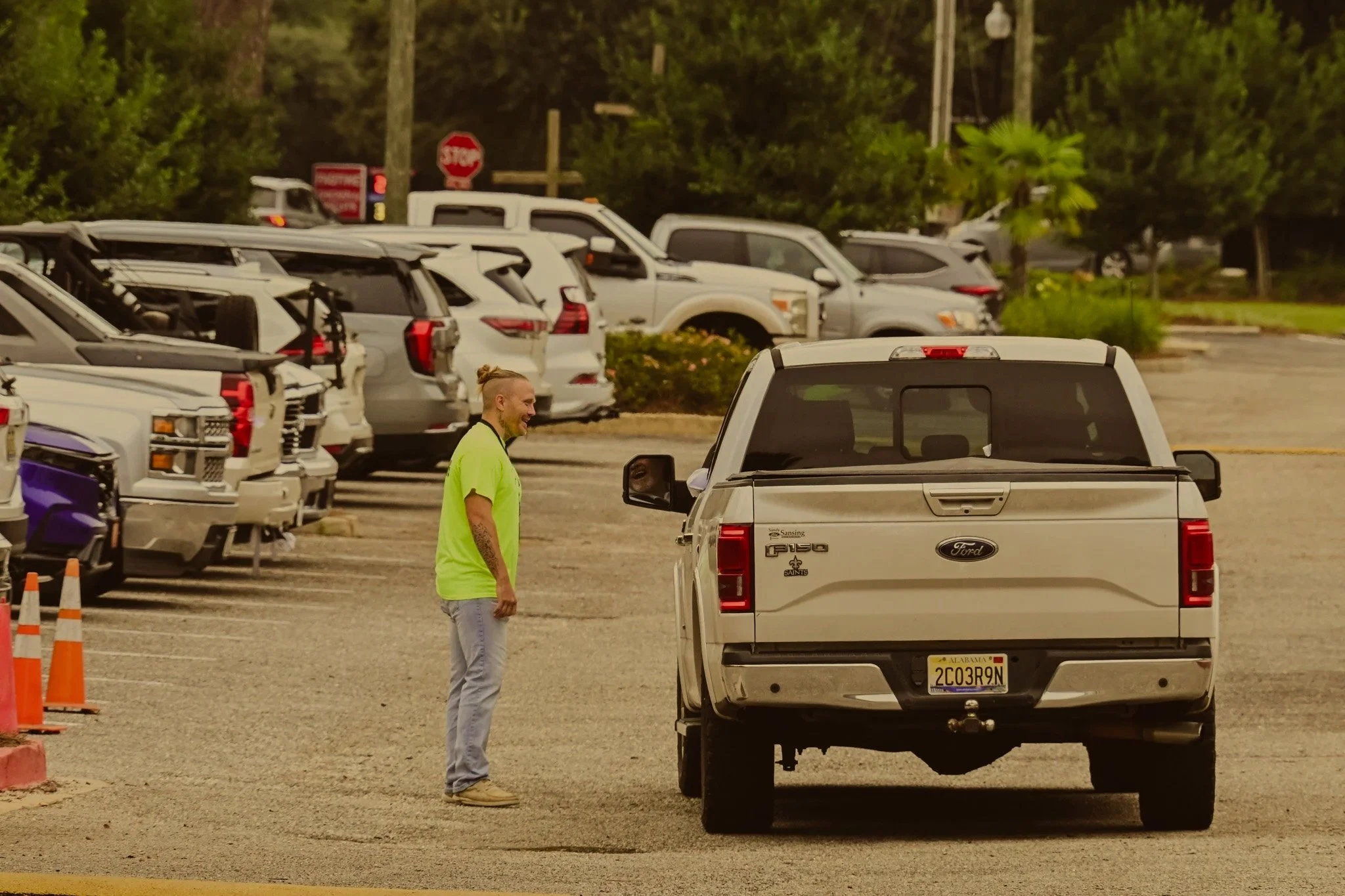 Man in a yellow shirt is smiling and standing in a parking lot talking to someone in a white truck.